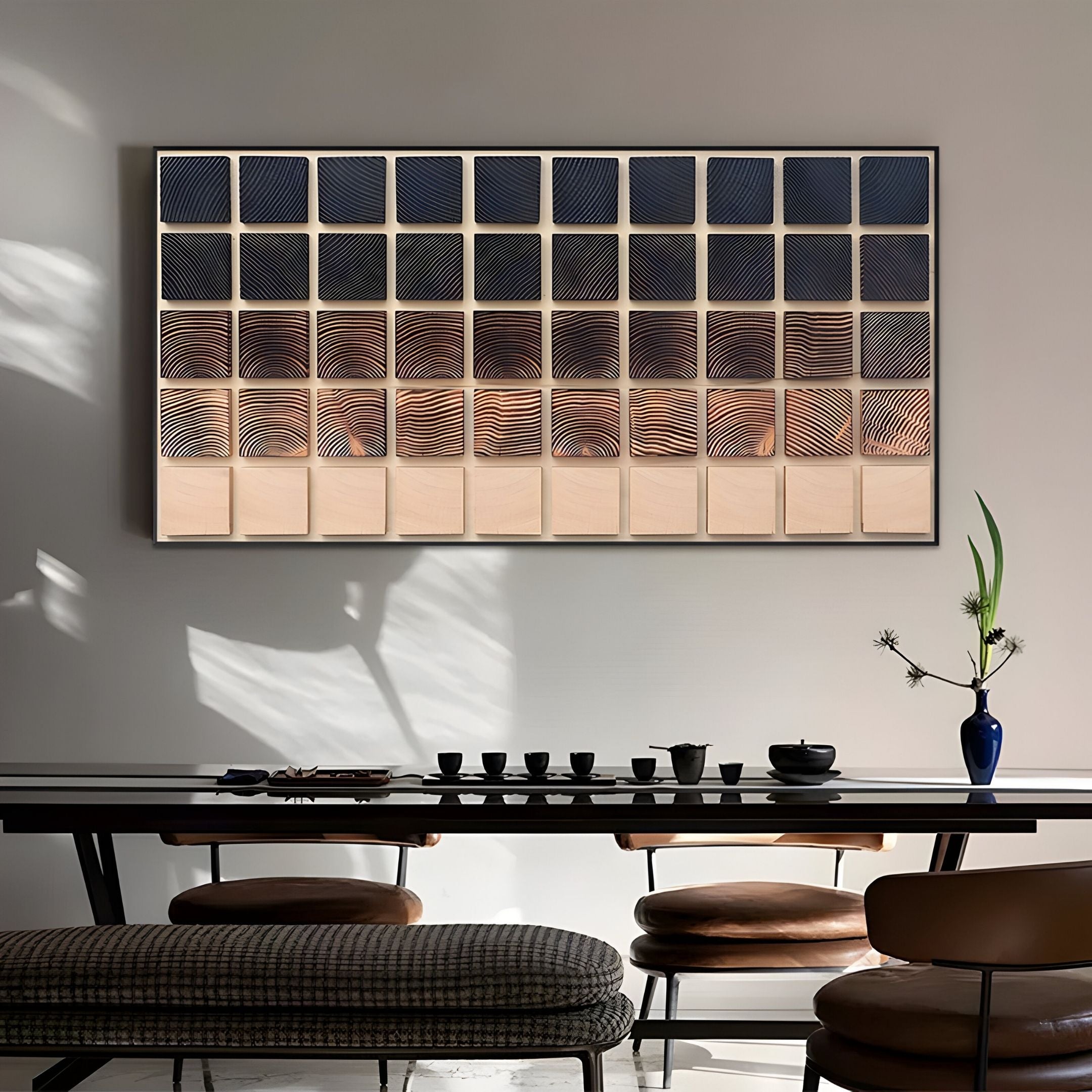 A modern dining area features a wooden table set for tea, cushioned stools, and a blue vase with a single stem. The wall displays the Quadrelle Midnight & Sand Grid Geometric 3D Wall Art by Giant Sculptures.