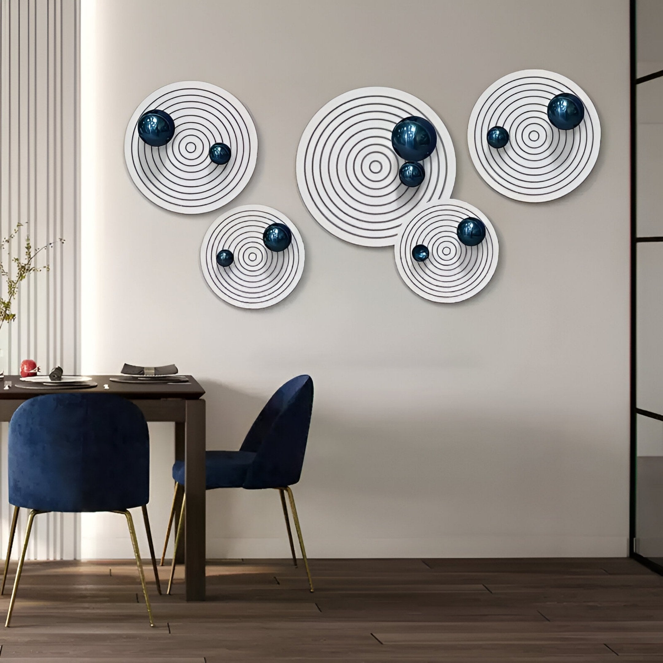 A modern dining area features navy velvet chairs, a wooden table, and Giant Sculptures' Orbiora Blue Orb 5-Panel Concentric Sphere 3D Wall Art. Light from the left highlights the glossy blue sphere design and enhances the contemporary decor.