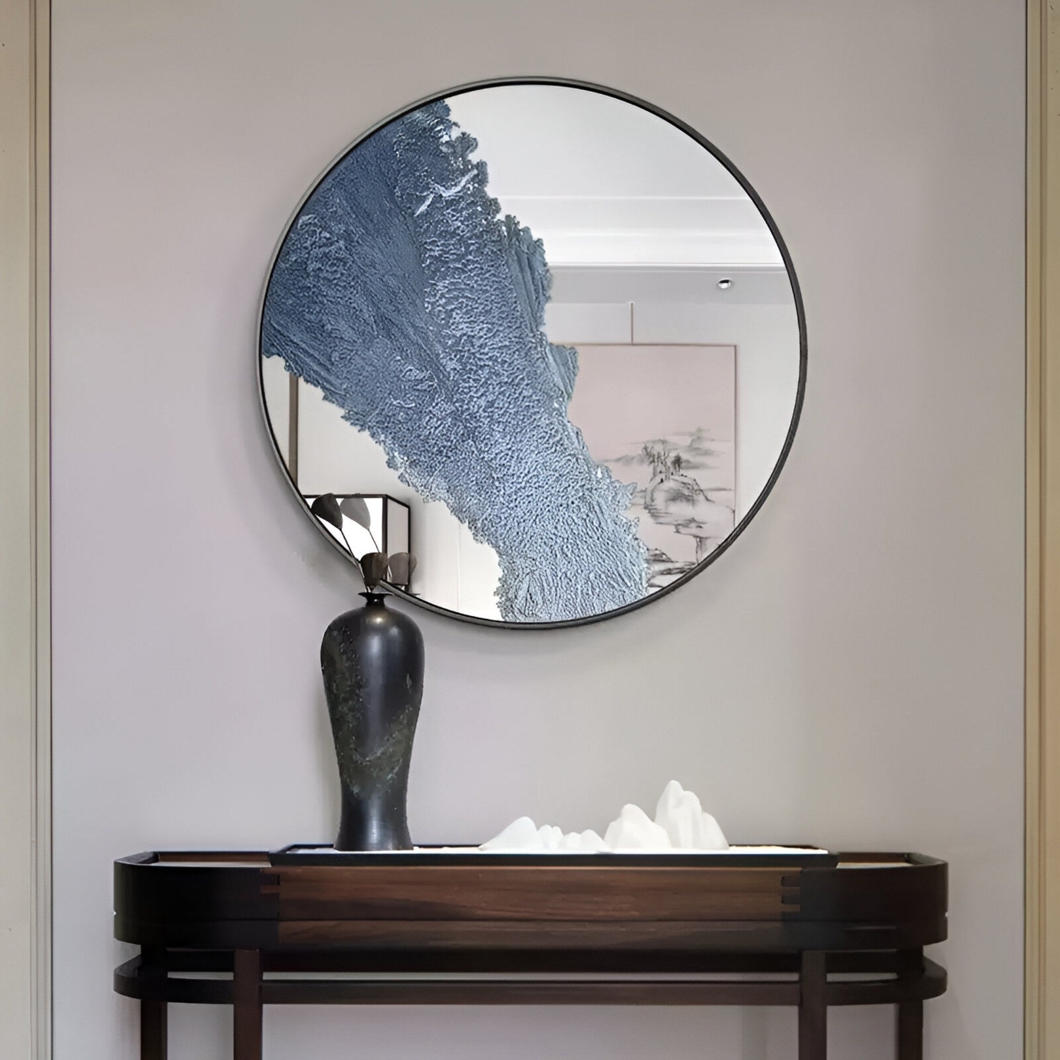 The Erosian Blue Flow Textured Round Mirror 3D Wall Art by Giant Sculptures hangs above a dark wooden console, paired with a black vase and white decor for a minimalist, contemporary look.
