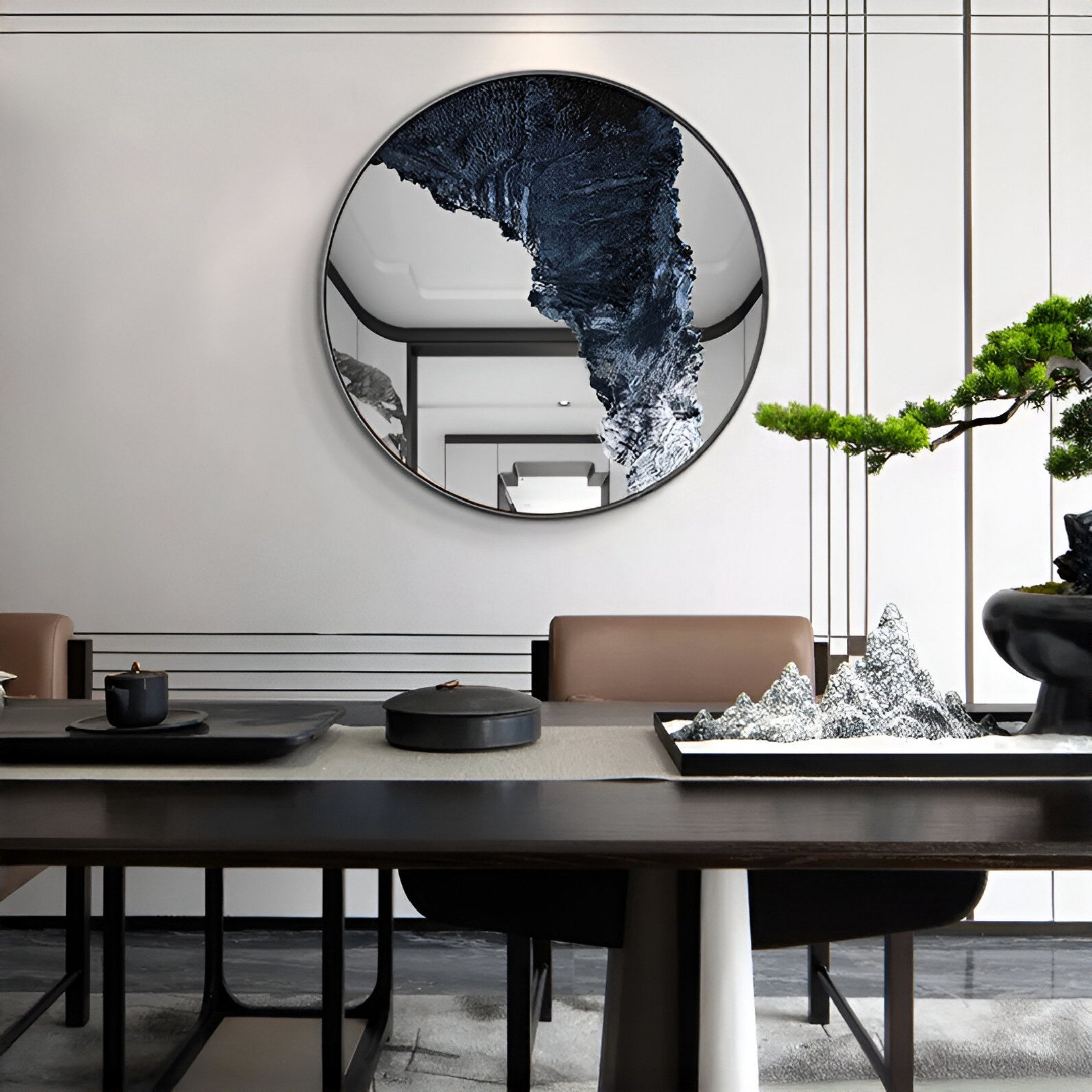 A modern dining room features the Giant Sculptures Erosian Midnight Stream Textured Round Mirror 3D Wall Art, minimalist furniture, a bonsai tree, and a decorative mountain-shaped sculpture on the table.