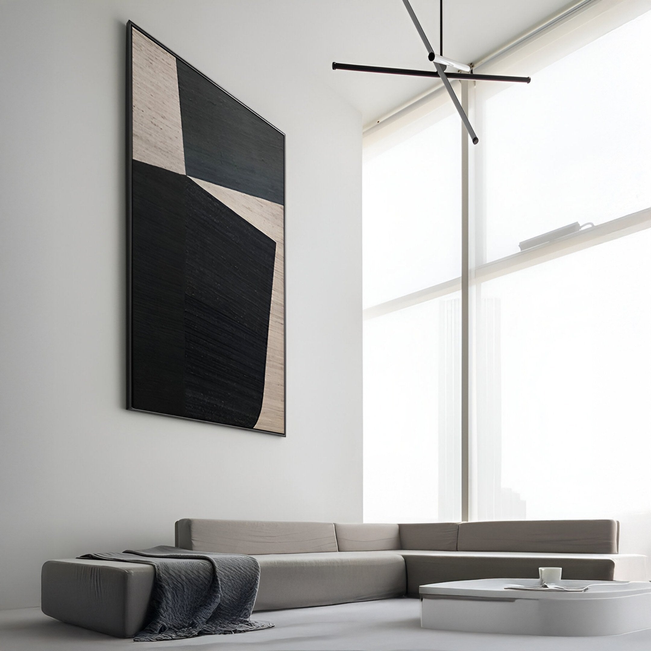 A minimalist living room featuring a light-gray sectional, round white coffee table, gray throw blanket, and the Striatura Slate Grey & Black Rope Abstract 3D Wall Art by Giant Sculptures. Large windows flood the space with light.