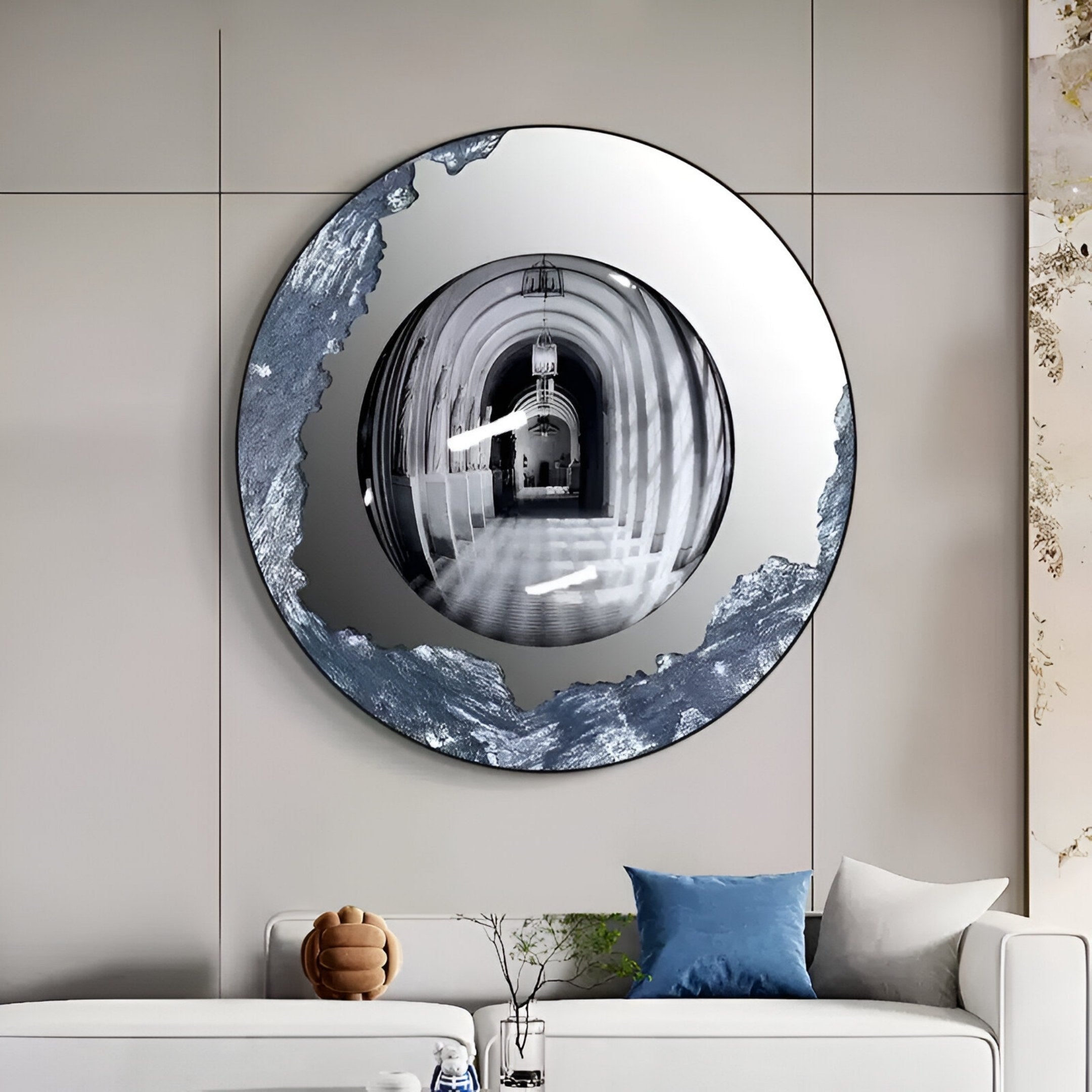 The Portara Silver Archway Illusion Round 3D Wall Art by Giant Sculptures, featuring a metallic, artistic border, hangs above a modern white sofa with blue and white cushions and a brown decor object in a contemporary living room.