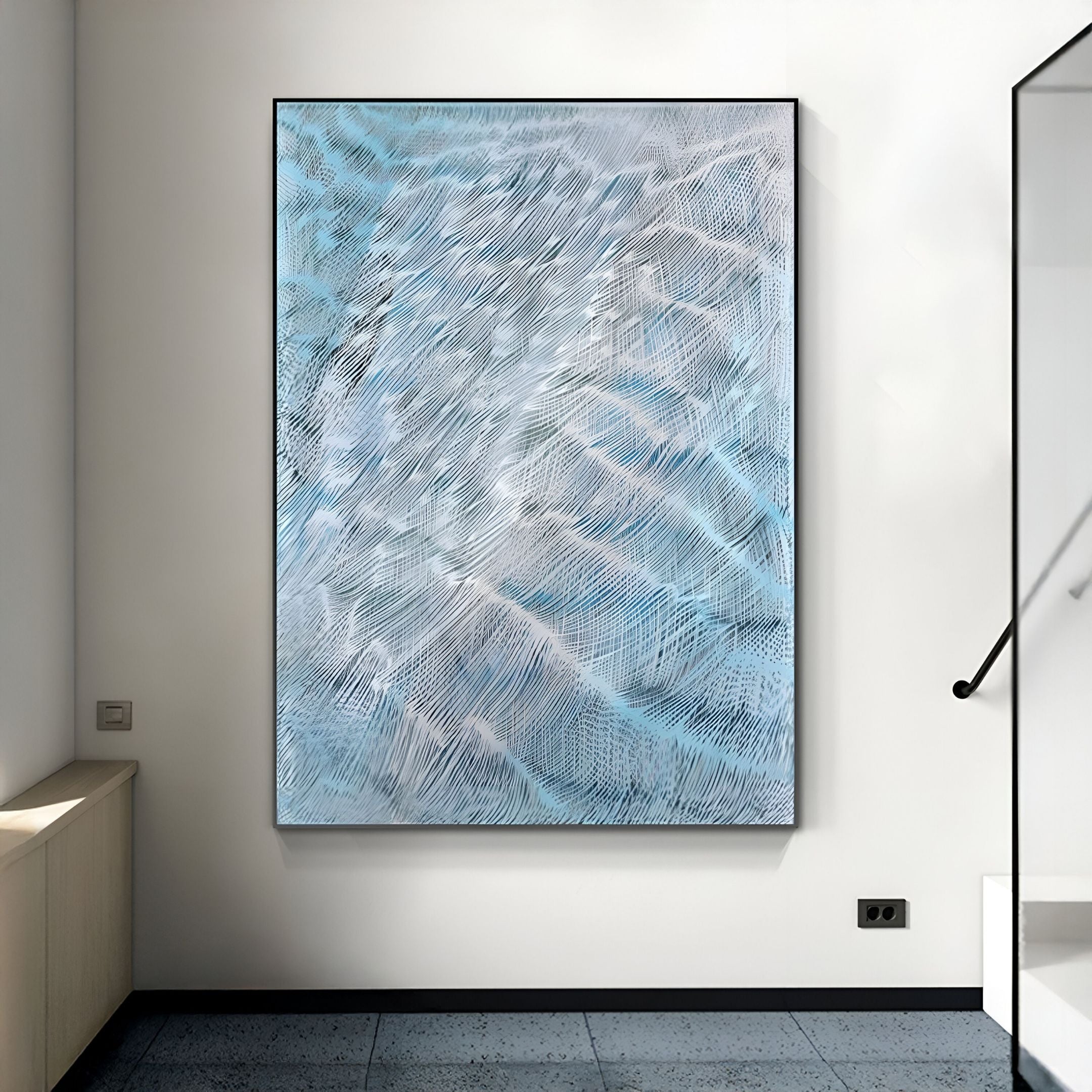 The Aqualis Blue Ripple Textured Abstract 3D Wall Art by Giant Sculptures, featuring blue with white and gray streaks, hangs on a white wall in a modern room with tiled floors and a staircase nearby.