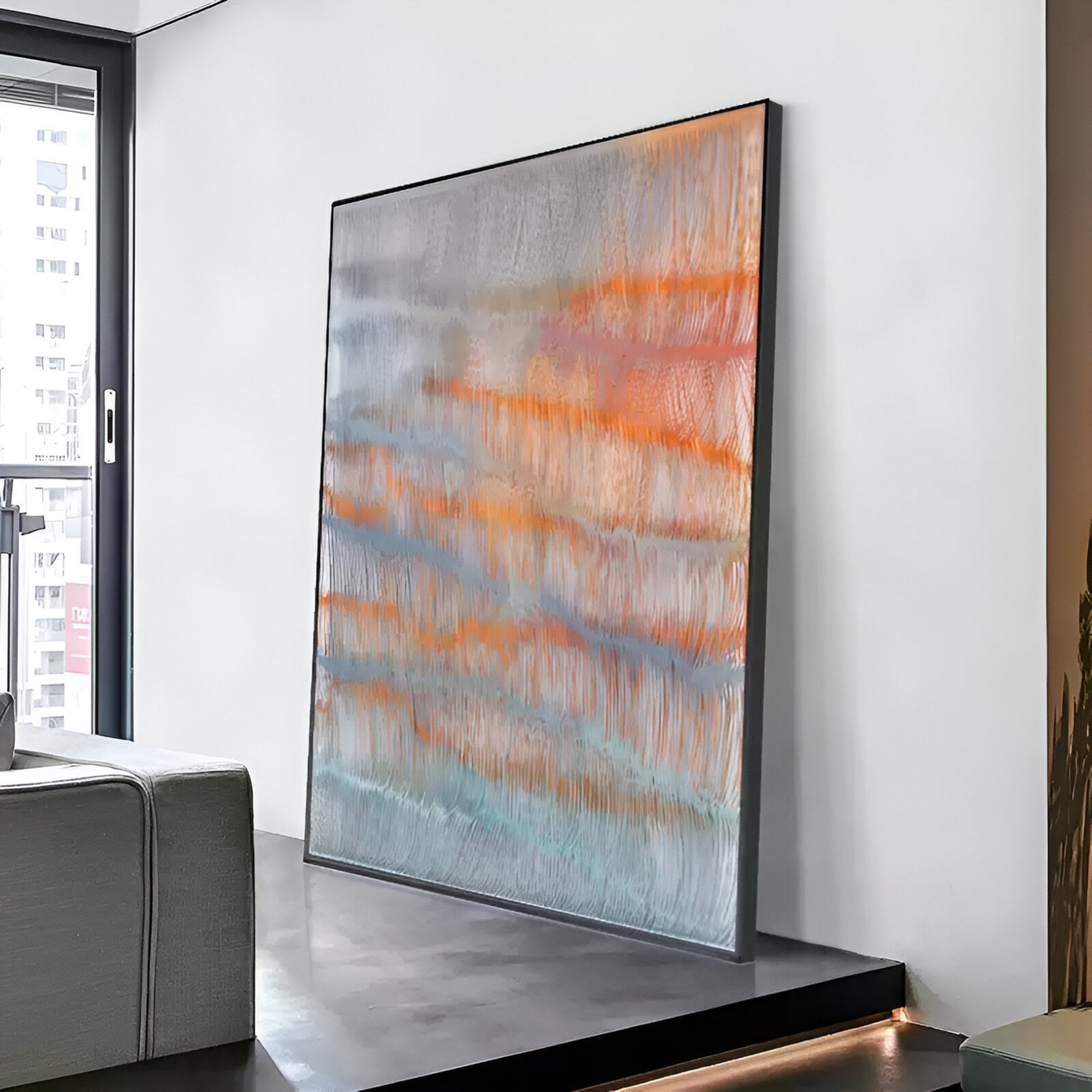 The Giant Sculptures Aqualis Sunset Orange & Blue Textured Abstract 3D Wall Art leans against a white wall on a dark platform in a modern, minimalistic room with large windows.