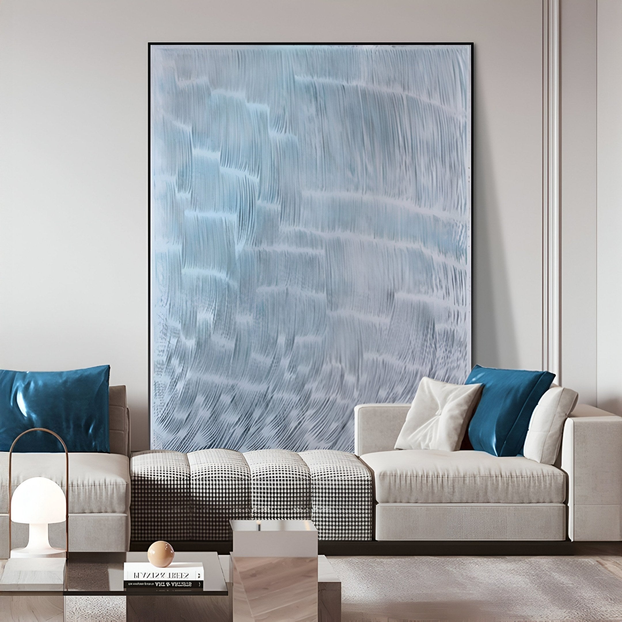 A modern living room features the Aqualis Frosted Ice Curve Textured Abstract 3D Wall Art by Giant Sculptures in blue and white, paired with beige sofas, blue and white cushions, a checkered throw, a white coffee table, and a side table lamp.