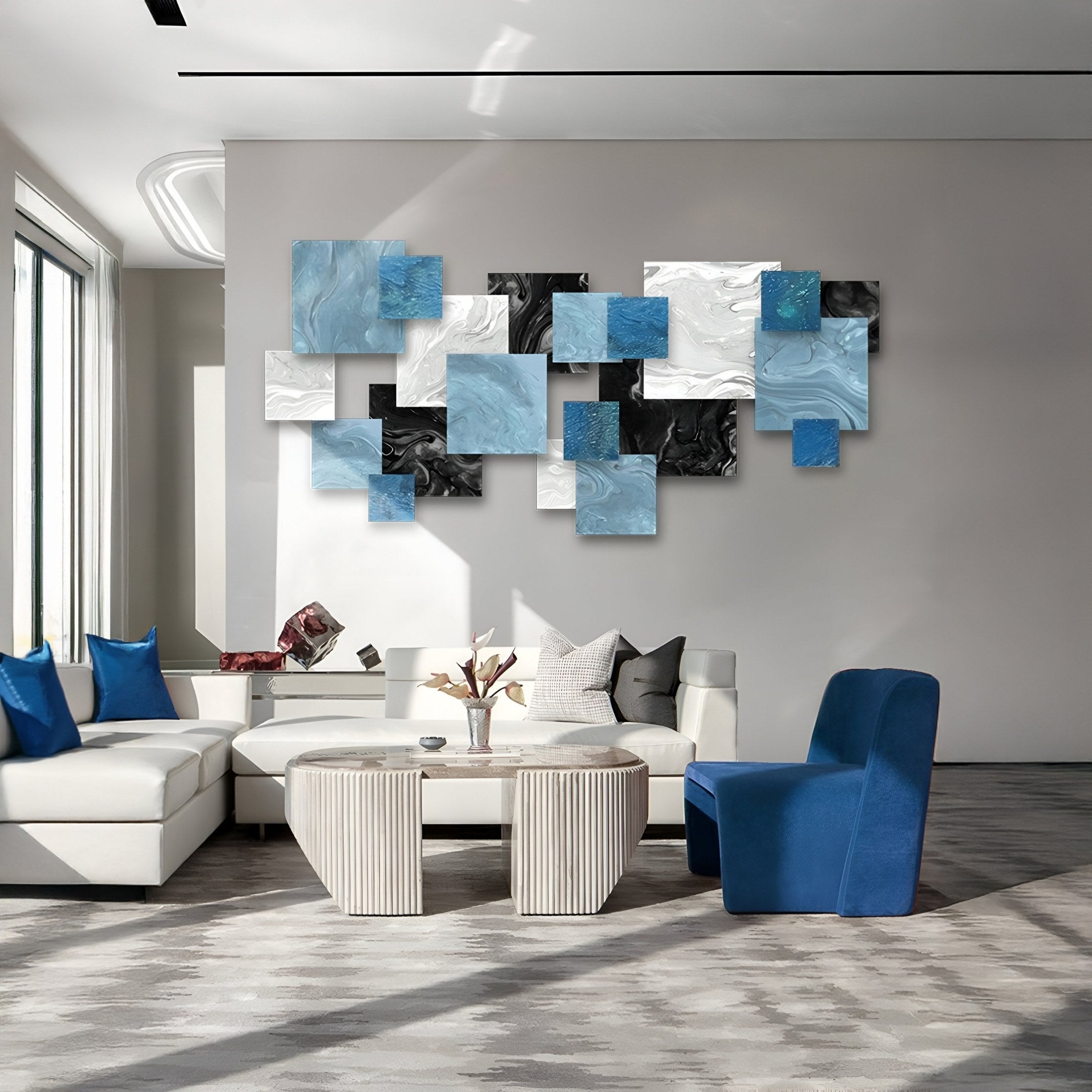 A modern living room features white sofas, a blue chair, two ribbed round coffee tables, and the Stravane Blue & Black Mosaic Oil Canvas 3D Wall Art by Giant Sculptures above the couch. Large windows fill the space with natural light.