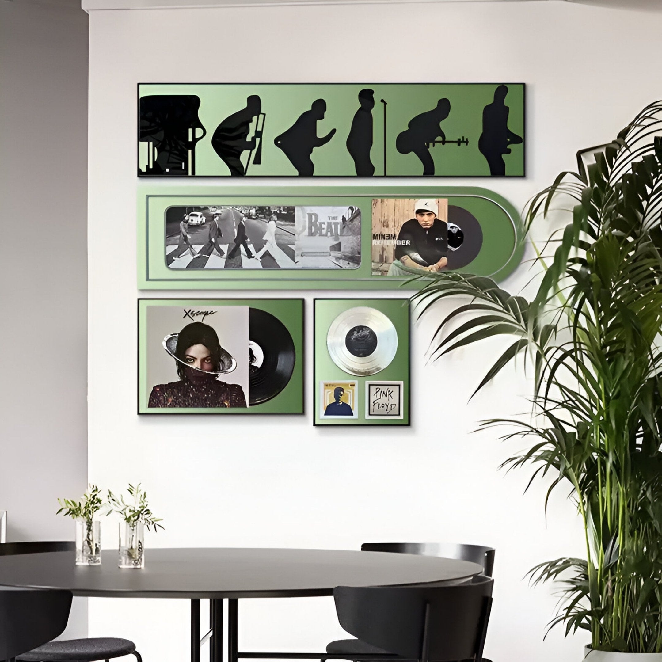 A modern dining area with a black table and chairs, featuring Giant Sculptures' Sonarta Green Multi-Panel Record & Silhouette Wall Art, Beatles Abbey Road art, music-themed decor, and a large green plant on the right.
