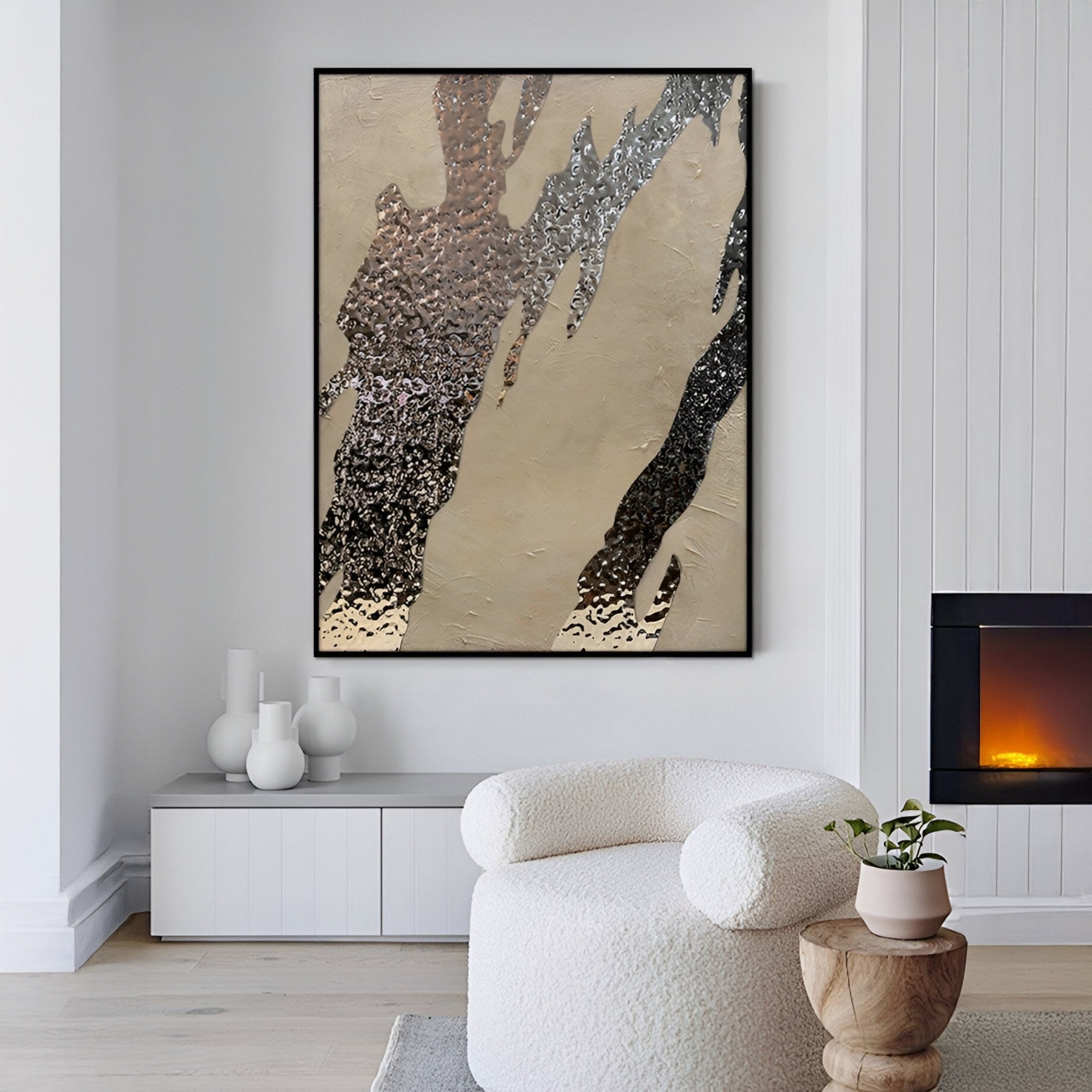 A modern living room features a white textured lounge chair, round wooden side table, and fireplace. Above a minimalist console with ceramic vases hangs Giant Sculptures’ Metallura Beige & Silver Metallic Flow Abstract 3D Wall Art.