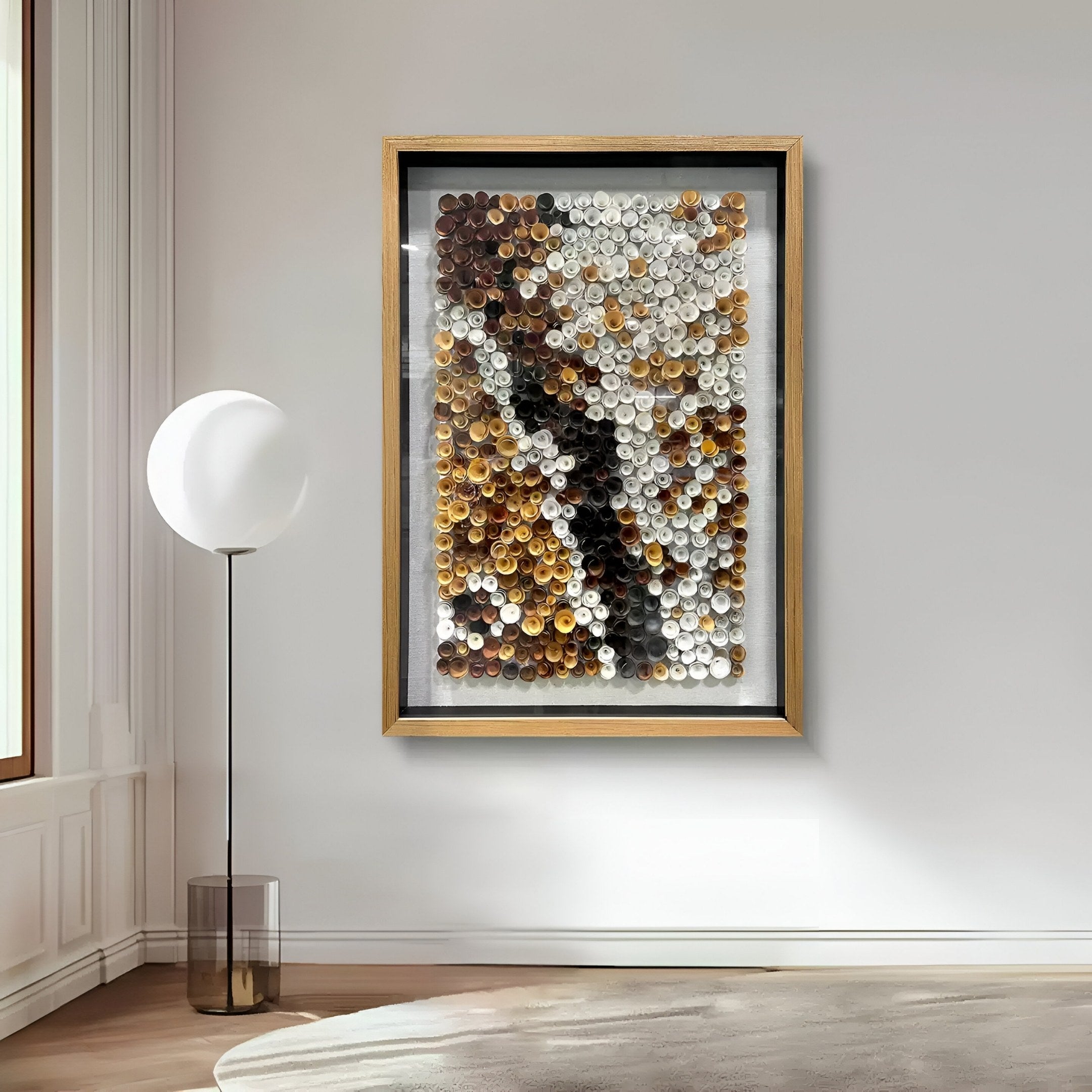 A modern living room showcases the Volaris Ochre & Ivory Rolled Floral Framed 3D Wall Art by Giant Sculptures, featuring rows of colored circles in brown, gold, white, and black tones on a light wall beside a round white floor lamp.