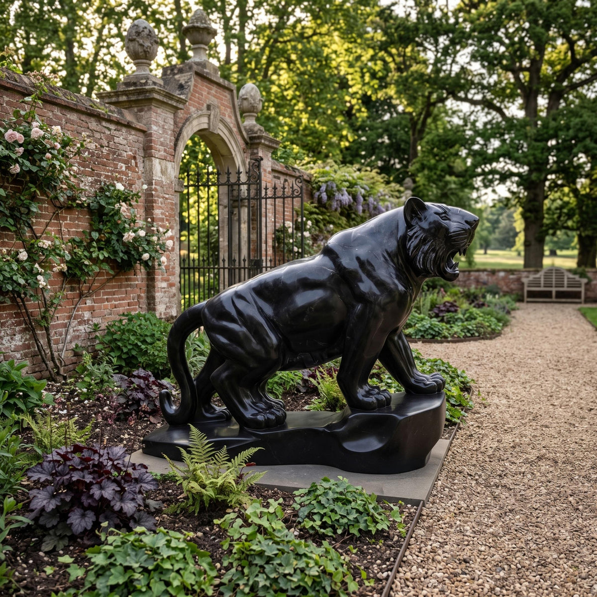 Prowling Tiger Black Marble Statue - 150cm, mirror-polished with grey mottling, jaws open, set on a garden path near a brick wall and iron gate.