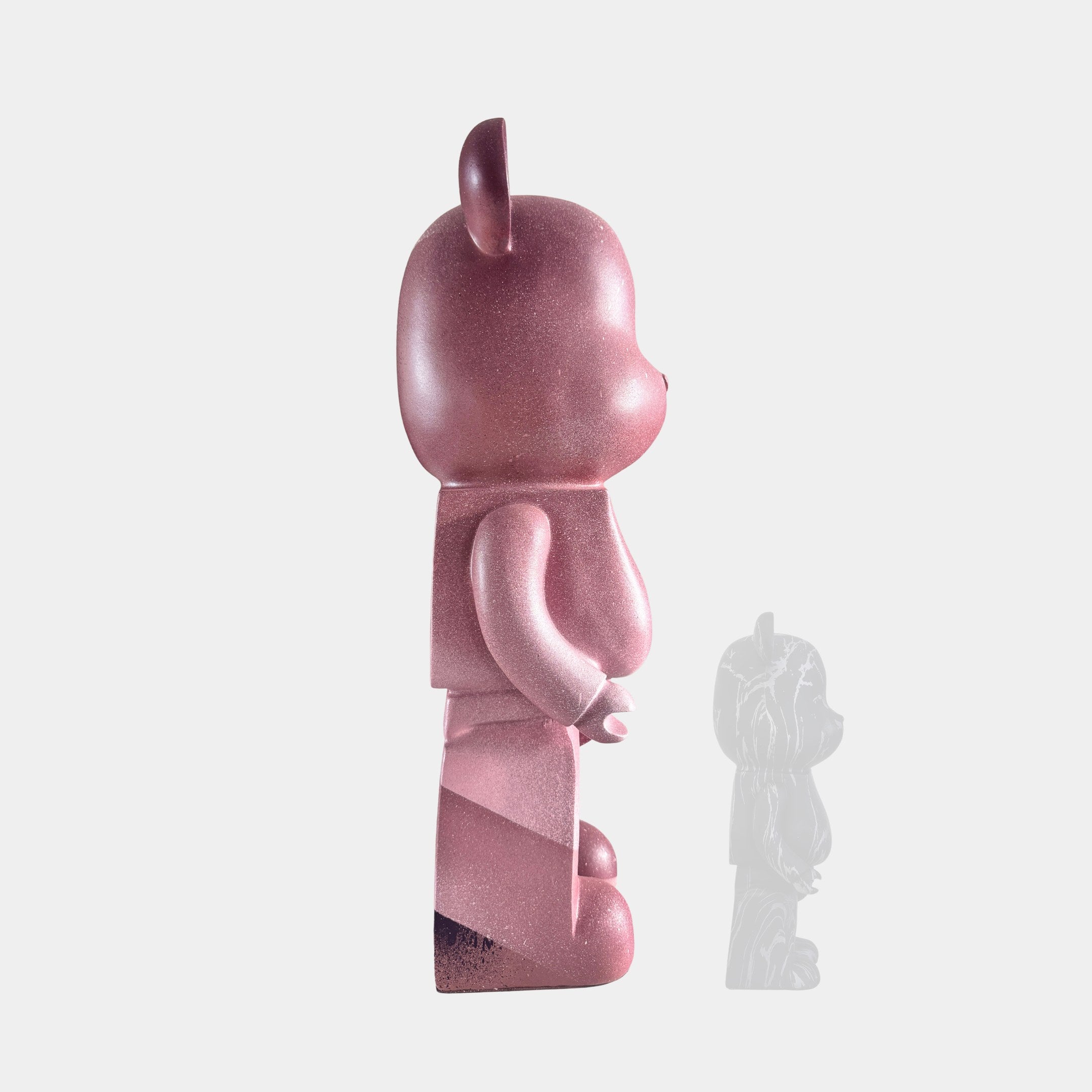 The Giant Sculptures Pinque Bear Sculpture - 50cm, in shiny pink, stands upright in profile on a white background. A small, semi-transparent version of this limited edition piece appears near its feet, overlapping the shadow.