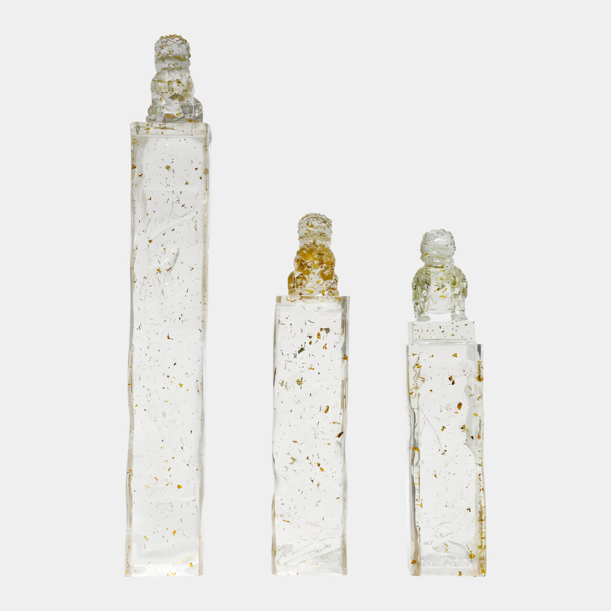 Clear Gold-Flecked Guardian Lion Resin Pillar in three heights (89/96/140cm), each clear column with scattered gold flakes topped by a forward-facing lion, on a plain white background.