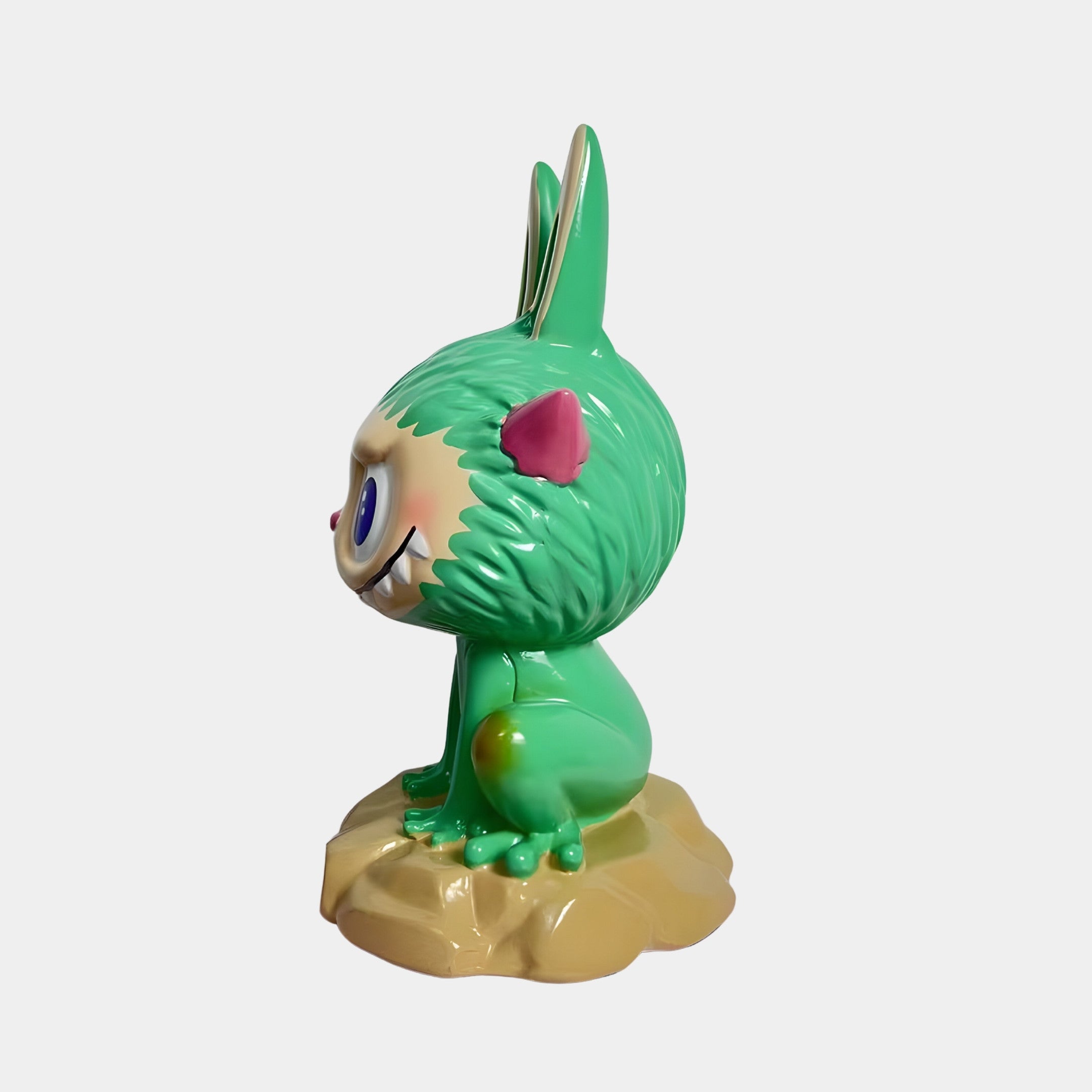 The Monster Frog Labubu Sculpture - 160cm by Giant Sculptures features a green, cartoon creature with pink, rabbit-like ears, large eyes, a big smile, alien bioluminescence, and sits on a tan rock-like base.