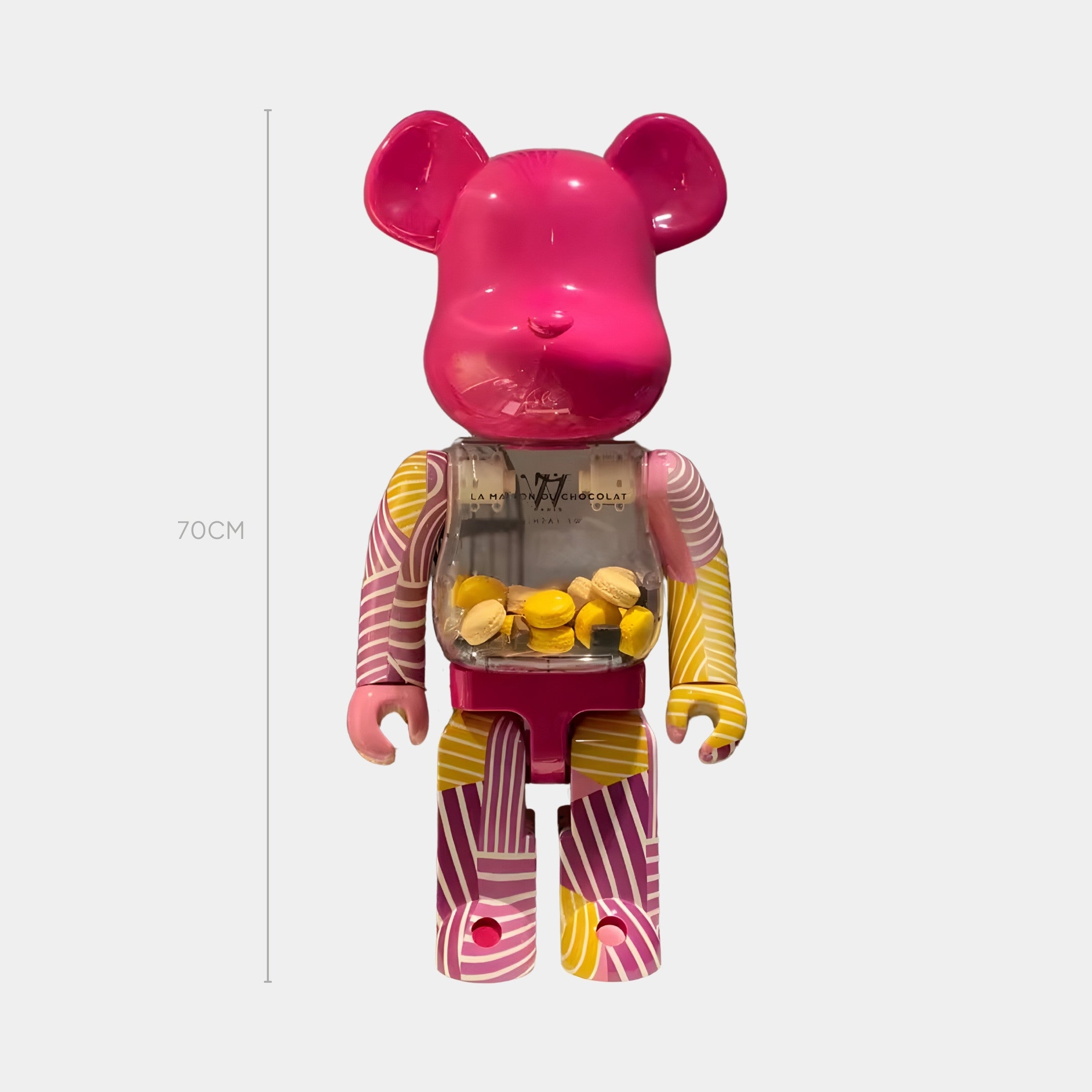 The Striped Carnival Bear Sculpture - 70cm by Giant Sculptures features a pink resin body with abstract yellow and white arm and leg patterns, plus a transparent chest filled with yellow and white capsules.