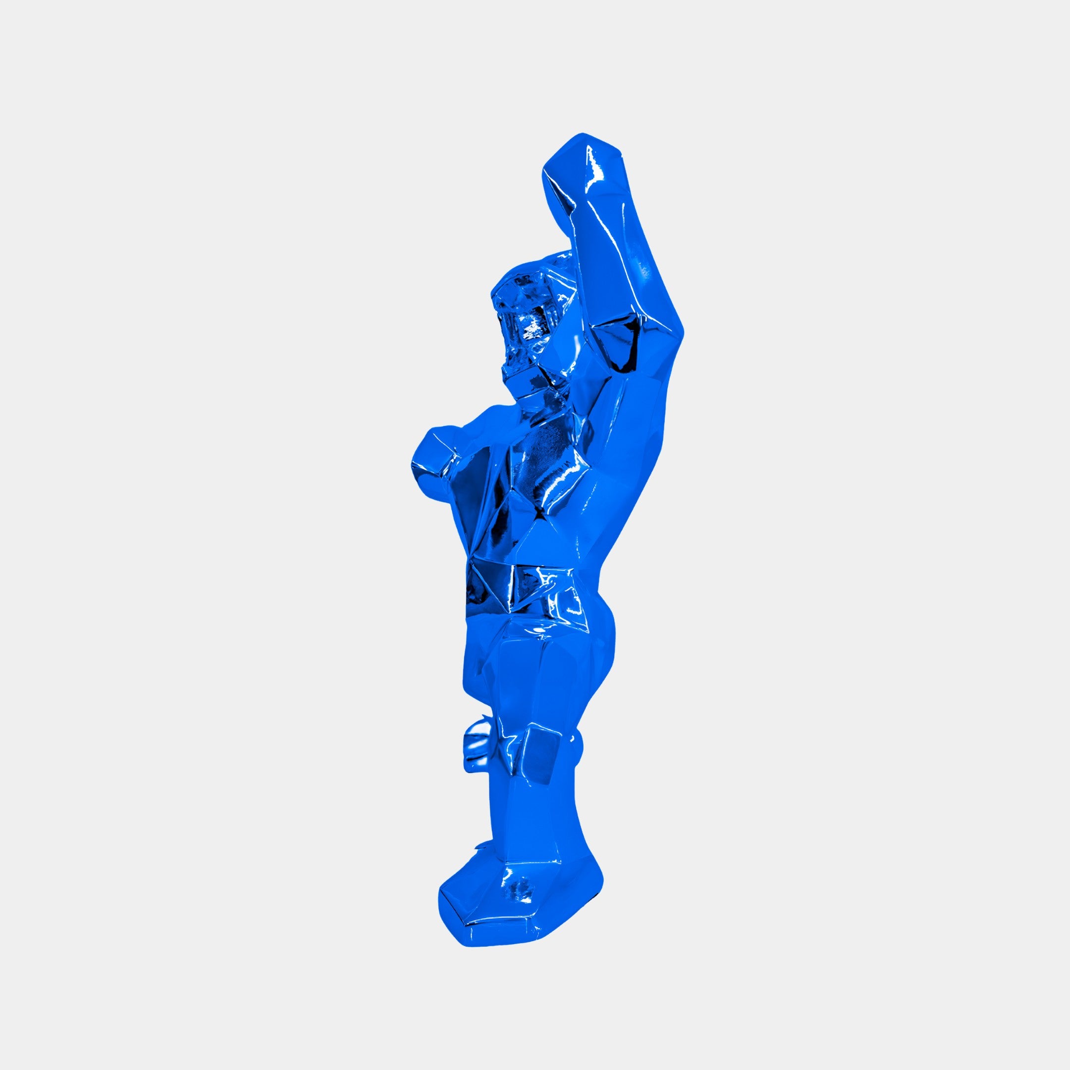 The Sapphire Blue Gorilla Sculpture - 50cm by Giant Sculptures stands upright with one arm raised. Its angular, geometric design creates an abstract look against a plain white background, emphasizing its vibrant color and unique shape.