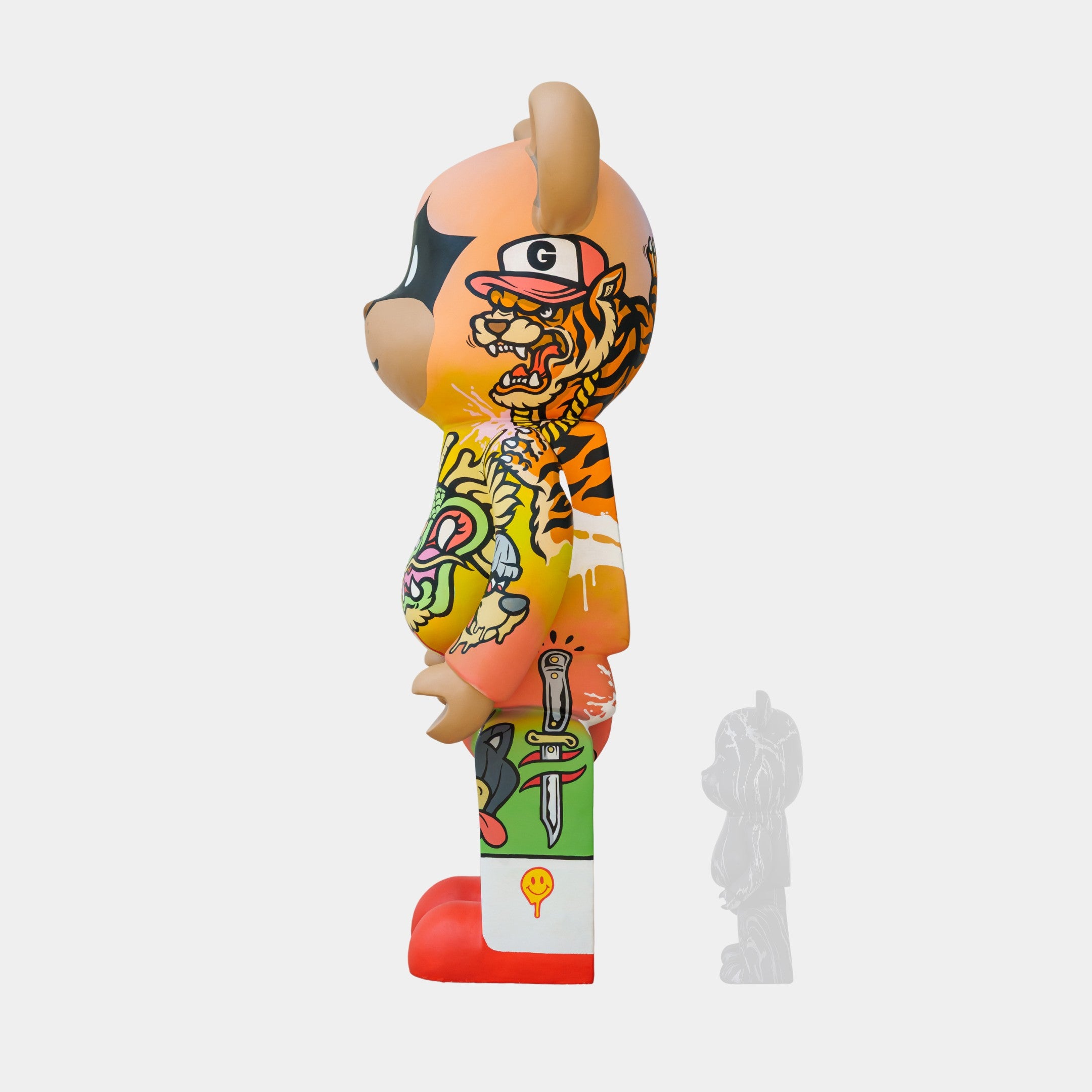 Side view of the vibrant Lucky Paws Bear Sculpture - 165cm by Giant Sculptures, a limited-edition piece inspired by Thai street art. This colorful bear has dragon and smiley face tattoos, a large round head, red shoes, and is accompanied by a small gray figurine on a plain white background.