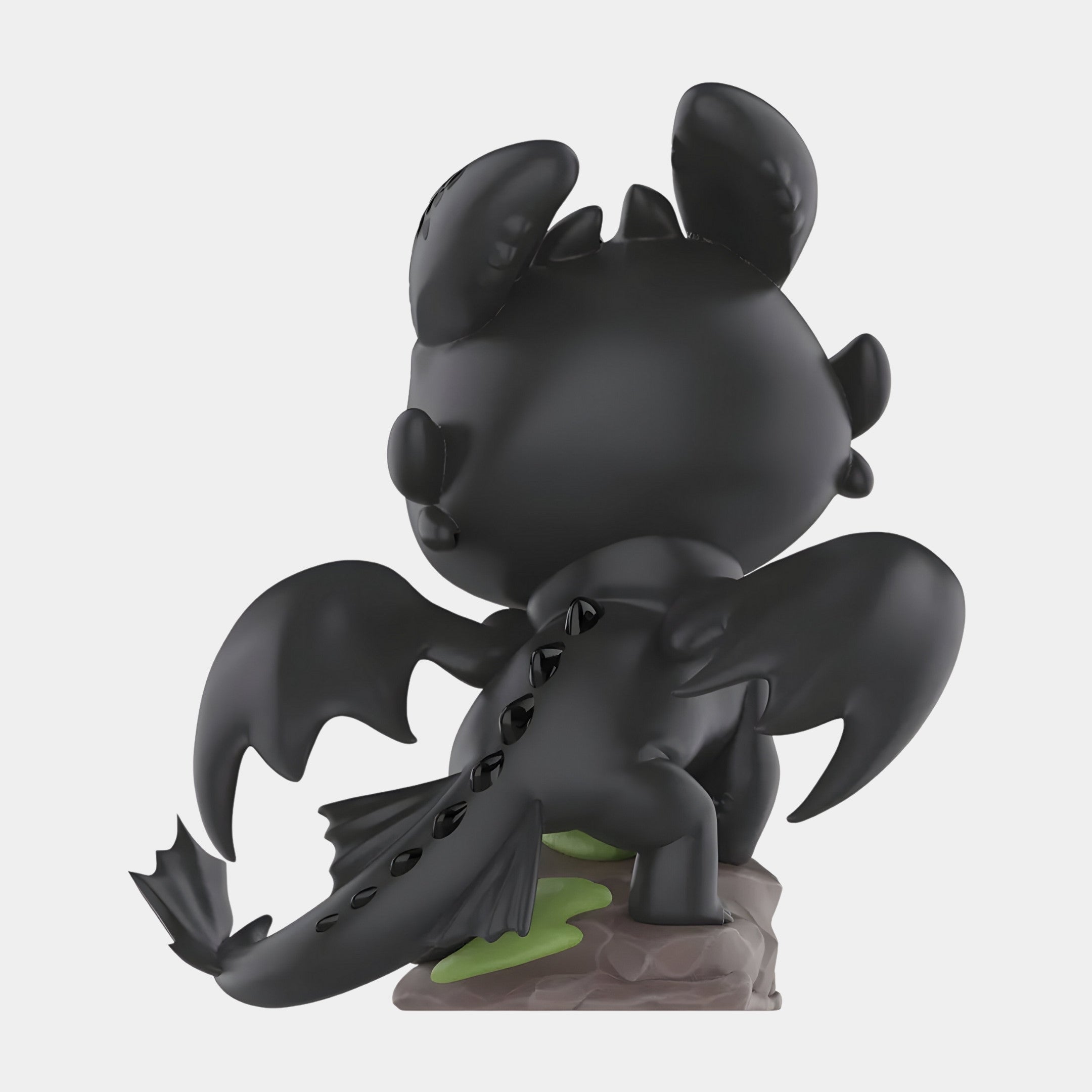 The Dragon Bond Toothless Labubu Sculpture by Giant Sculptures is a 160cm fantasy-themed vinyl art figure of a black dragon with large wings and a spiked tail, standing on grass-covered rock, facing away.