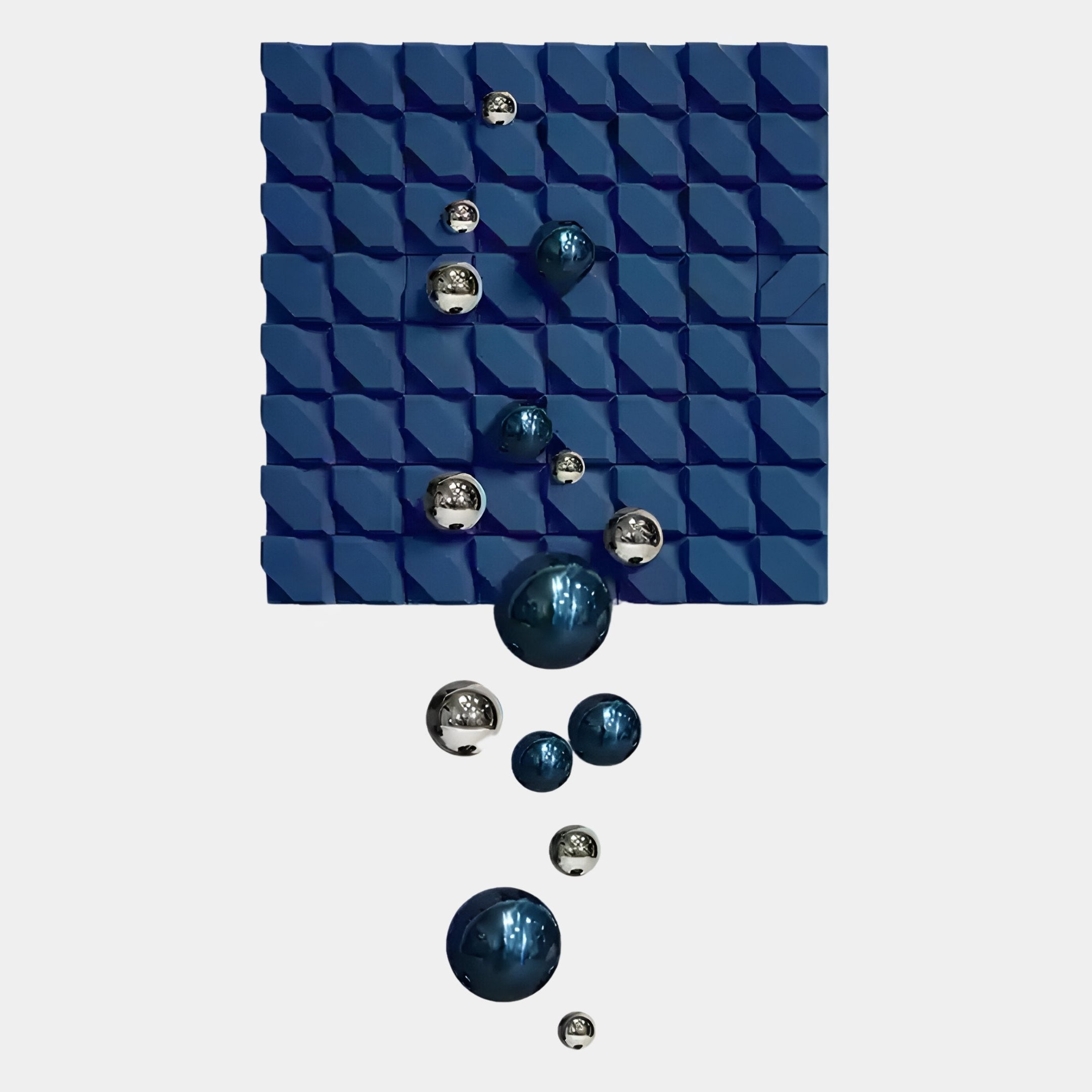 A blue textured square panel, similar to the Orbina Blue 3D Wood Relief Wall Art With Metal Ball by Giant Sculptures, is mounted on white with shiny silver and blue reflective spheres of different sizes cascading down in a unique arrangement.