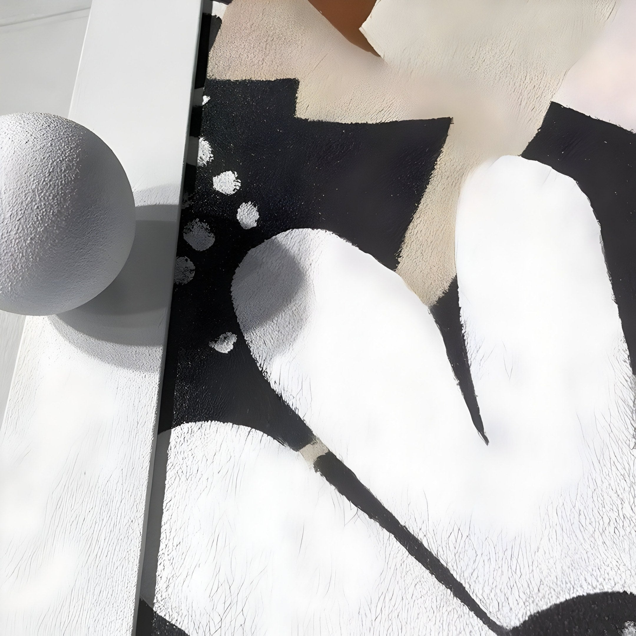 Close-up of the Florere Neutral Bloom Hand-Painted Sandstone 3D Wall Art by Giant Sculptures, featuring black, white, and beige patterns with a large soft-edged white shape on a black background. A textured white sphere casts a shadow on a light surface nearby.