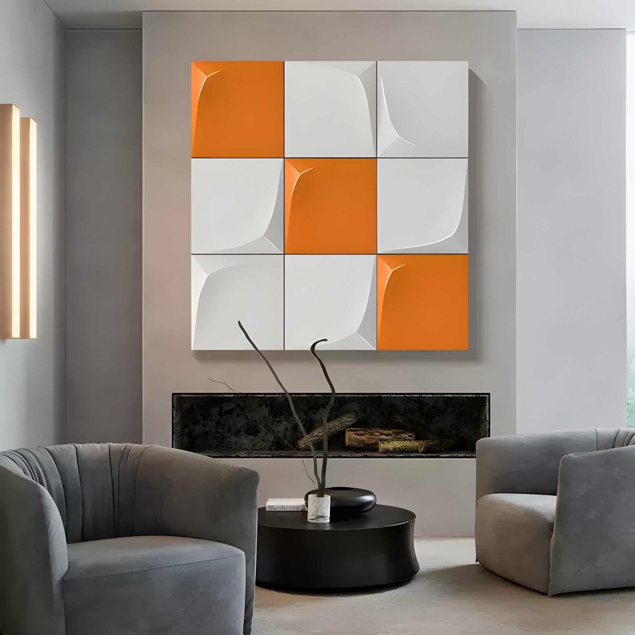A modern living room with gray walls features the Curvatura White & Orange Grid 3D Wood Relief Wall Art by Giant Sculptures. Two gray armchairs flank a round black table with a decorative branch vase, while a narrow wall-mounted fireplace below adds warmth to the space.