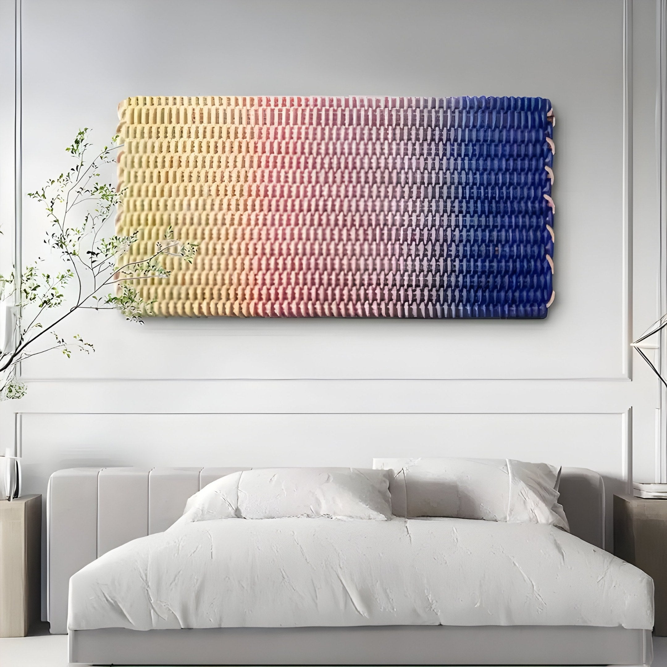 The Spectrum Weave Horizontal Sunset Hues Wood Relief 3D Wall Art by Giant Sculptures displays a tranquil sunset gradient from yellow to blue above a modern white bed, with sparse greenery and minimal decor enhancing the serene atmosphere.