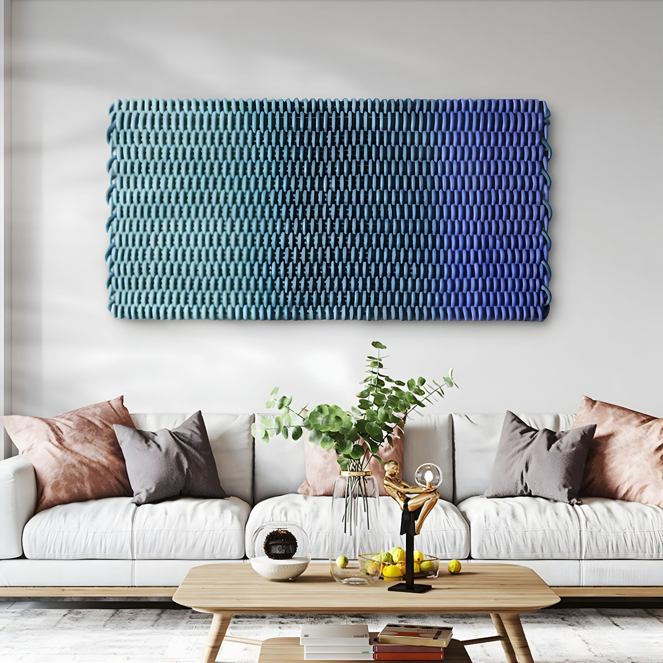 A modern living room showcases a white sofa with pink and gray cushions. A wooden coffee table holds decorative items. Above the sofa hangs Giant Sculptures Spectrum Weave Horizontal Midnight Blue Wood Relief 3D Wall Art, featuring transitions from teal to vibrant hues. A potted plant adds greenery.