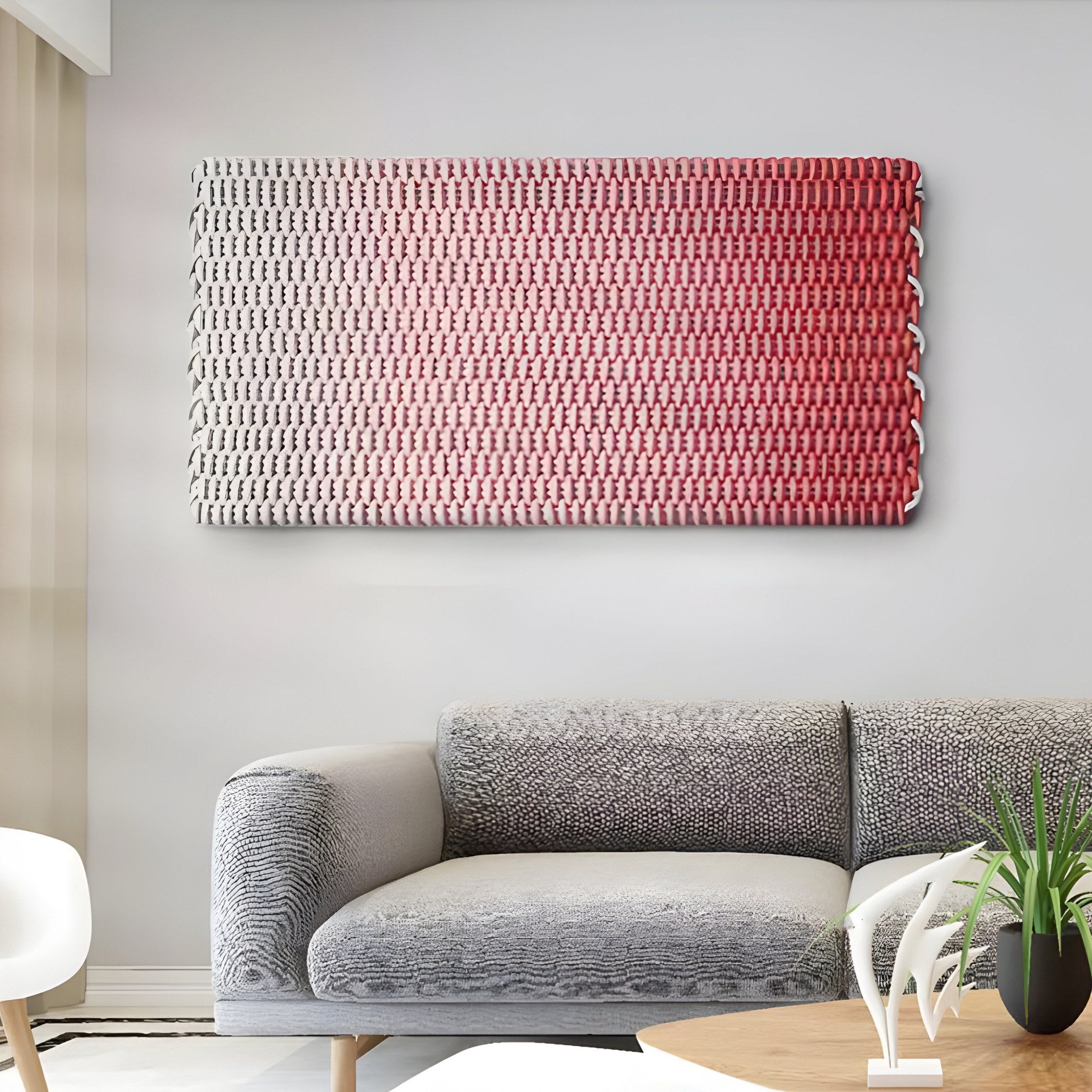 A modern living room showcases a gray textured sofa against a light wall, highlighted by Spectrum Weave Horizontal Rose Blush Wood Relief 3D Wall Art by Giant Sculptures. Abstract woven art in red and white hues and a small wooden table with black metal base add texture, complemented by white decor pieces for coziness.