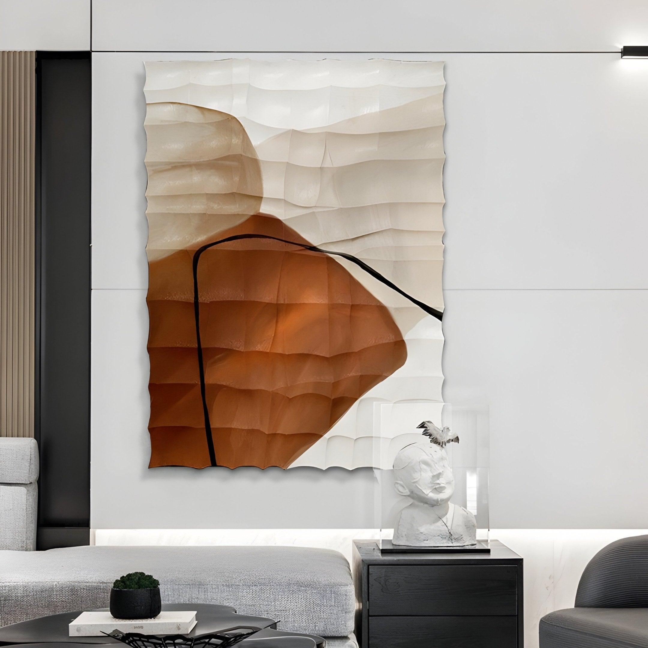 A modern living room features the Terracurve V Hand-Painted Sandstone Wood Relief 3D Wall Art by Giant Sculptures, showcasing wavy textures in brown and beige. Below, a bust in a glass case sits on a white shelf. A gray sectional sofa is paired with a small black table.