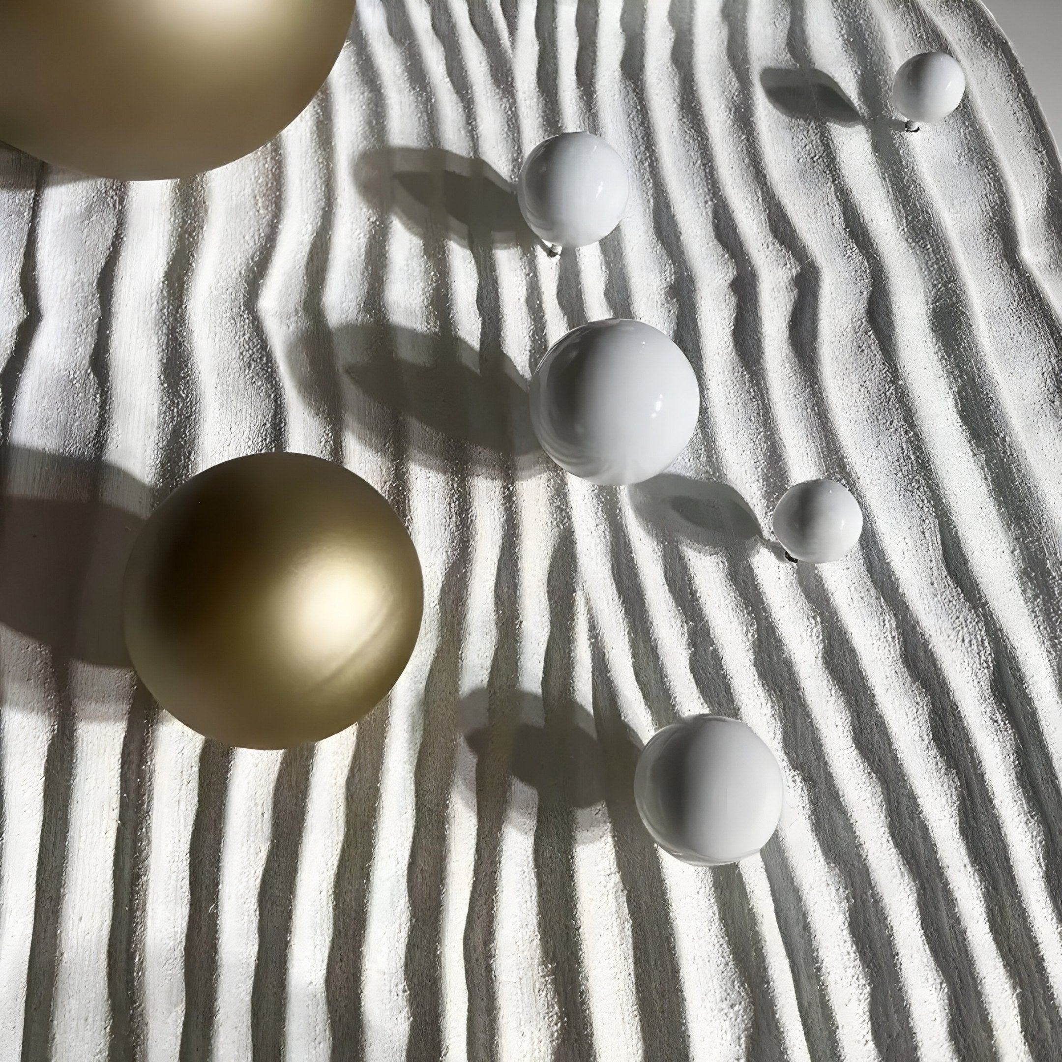 Giant Sculptures Lustra Gold & White 3D Wood Relief Wall Art With Metal Ball features gold and white metal balls on a wavy, textured white surface. Soft shadows and lighting enhance their minimalist elegance, reminiscent of refined wall art.