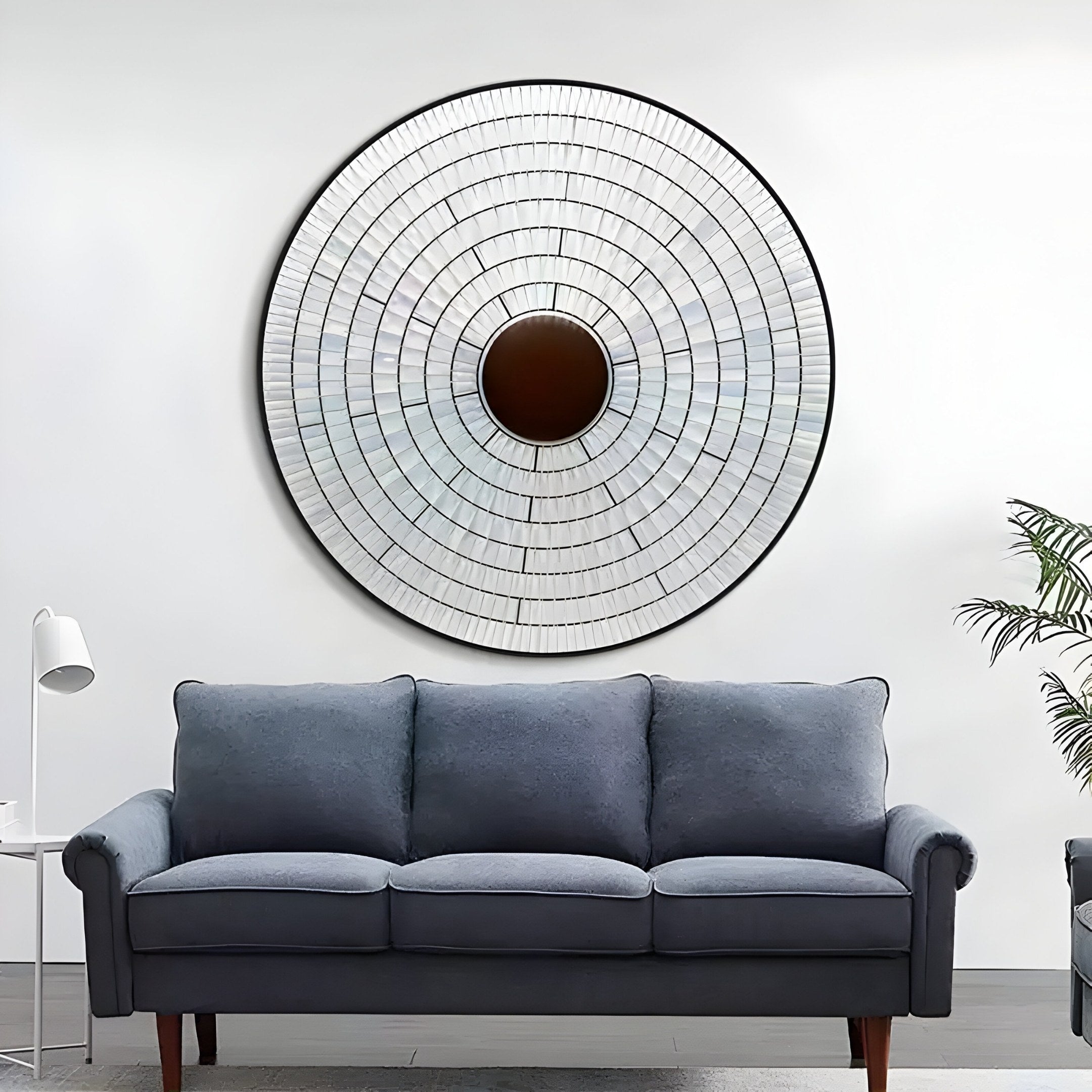 The Solis Radiant Deep Red Core Wood Relief 3D Wall Art by Giant Sculptures is mounted on a white wall above a blue-gray sofa, accompanied by a small white lamp on the left and a partially visible green plant on the right.