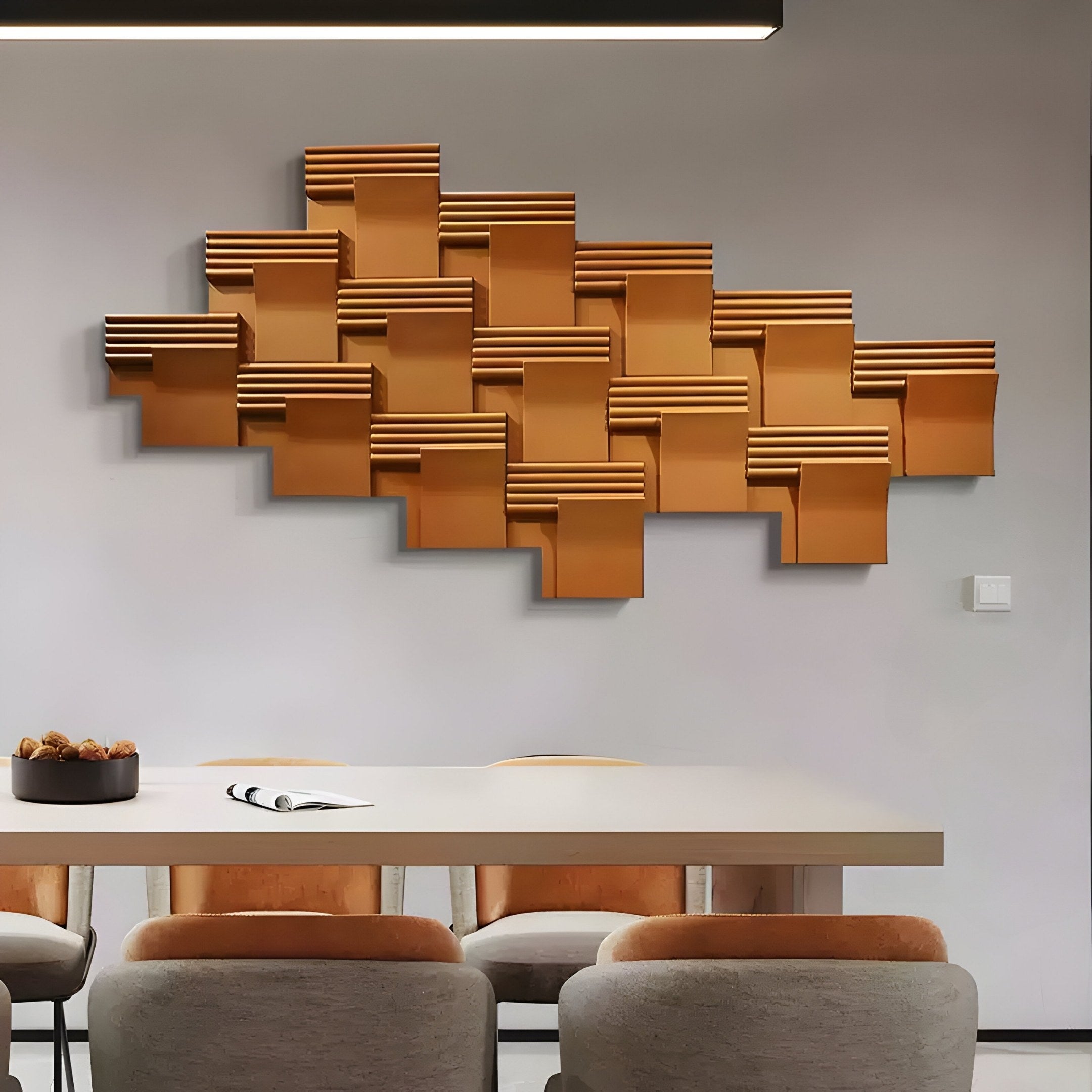 The Giant Sculptures Axura Brown Geometric Wood Relief Hand-Painted 3D Wall Art adds contemporary flair to the dining area. Below, a light wood table with four gray and orange chairs sits elegantly, complemented by a notebook and decorative bowl against neutral walls and sleek lighting.