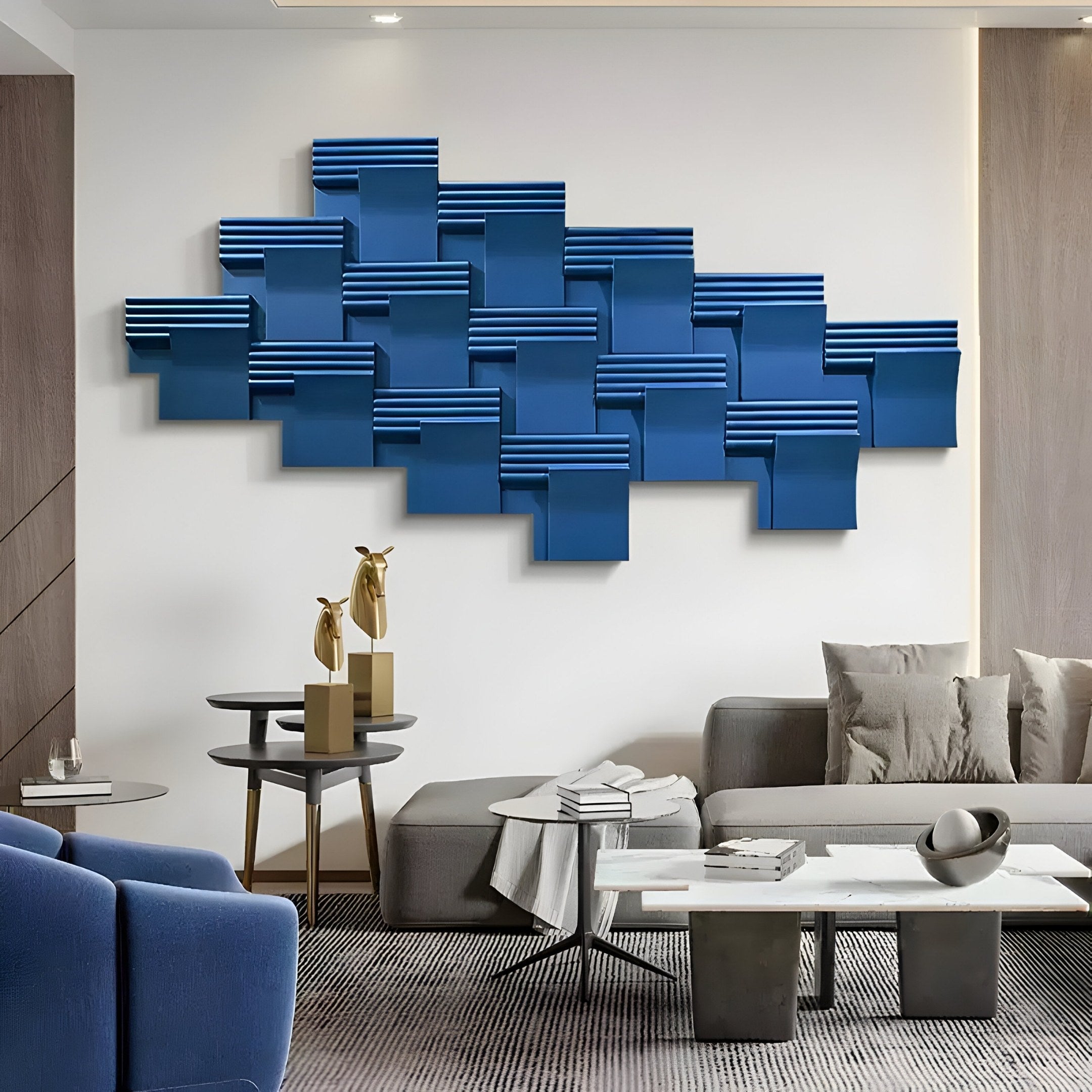 A modern living room features the stunning Axura Blue Geometric Wood Relief Hand-Painted 3D Wall Art by Giant Sculptures. It includes a gray couch with cushions, blue armchairs, small tables with gold decor, and is elegantly tied together with a monochrome rug.
