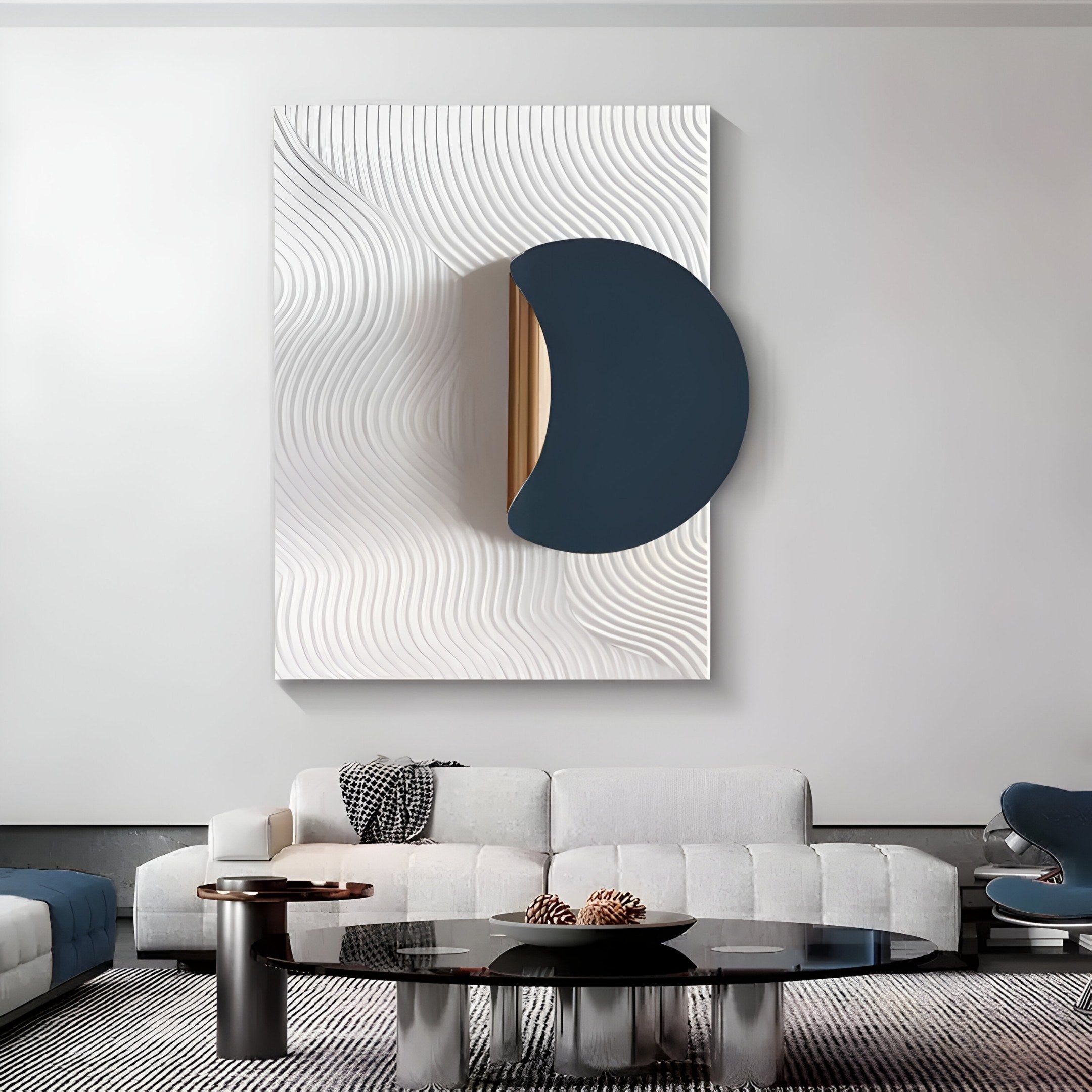 A modern living room features the Solvara Midnight Blue & White Wood Relief 3D Wall Art by Giant Sculptures, showcasing a dark crescent on a ripple background. Below, a minimalist white sofa with black and brown pillows faces a sleek black oval coffee table.