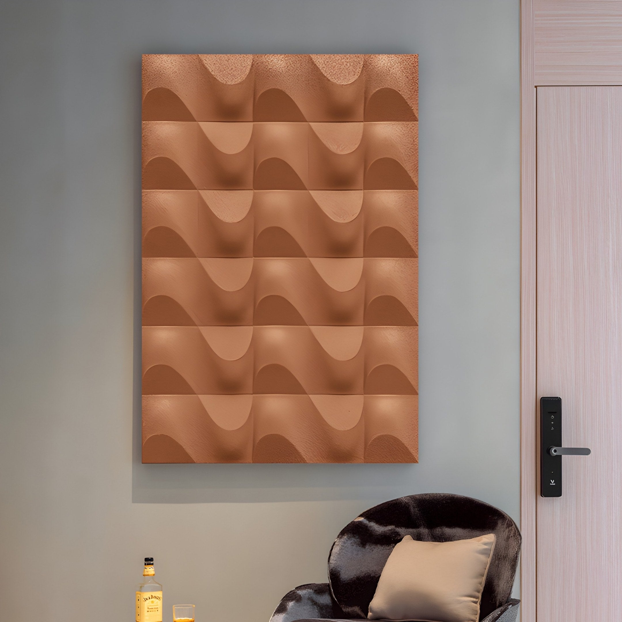 The modern room with gray walls features the Ondula Textured Earthy Wood Relief 3D Wall Art by Giant Sculptures, showcasing a grid of brown tiles. Below, a plush chair with a beige pillow sits by a door and a small table holding a bottle and glass.