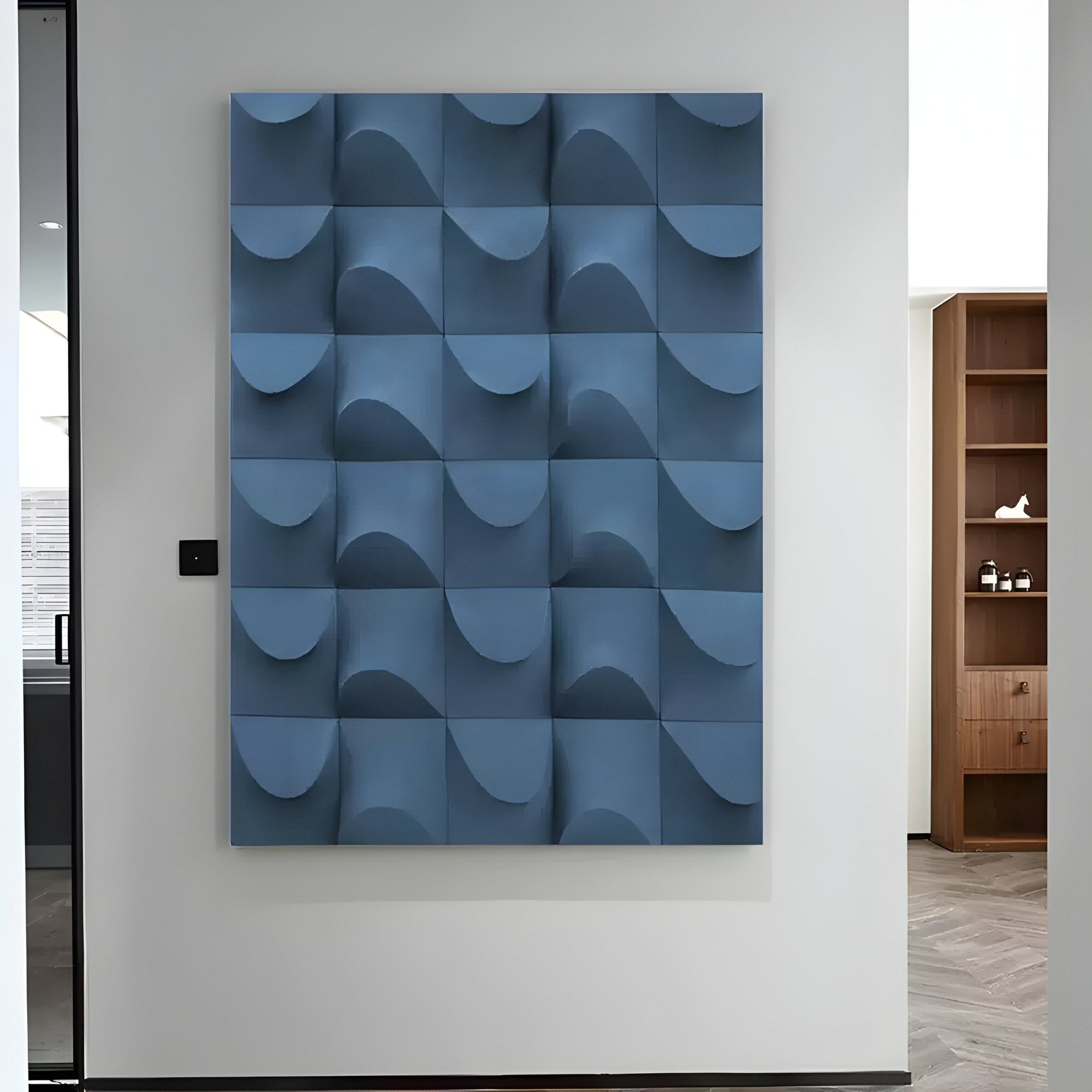 The Ondula Textured Blue Wood Relief 3D Wall Art by Giant Sculptures is a modern abstract piece featuring a grid of blue panels with wave-like patterns. It’s mounted on a light-colored wall, partially revealing a wooden bookshelf in the background.