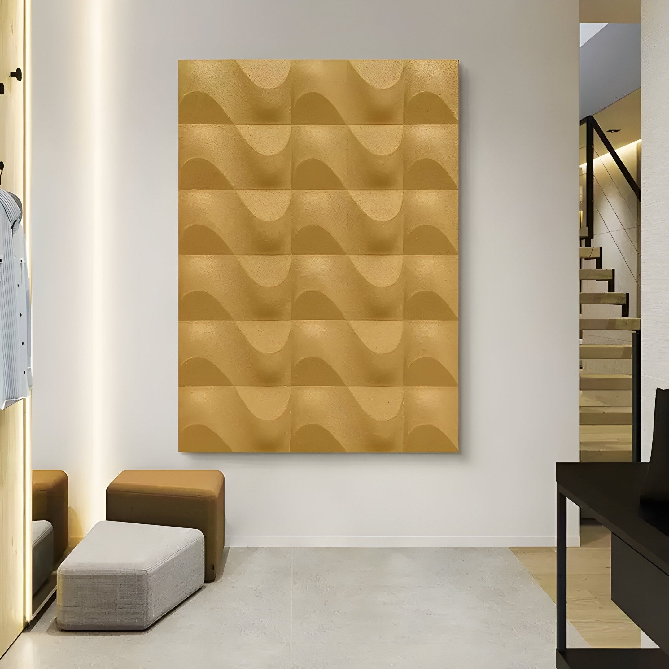A modern interior showcases the Ondula Textured Gold Wood Relief 3D Wall Art by Giant Sculptures, featuring abstract wavy patterns on white. Nearby, a curved staircase ascends, complementing a small seating area with a cushioned stool and chair on a light wood floor.