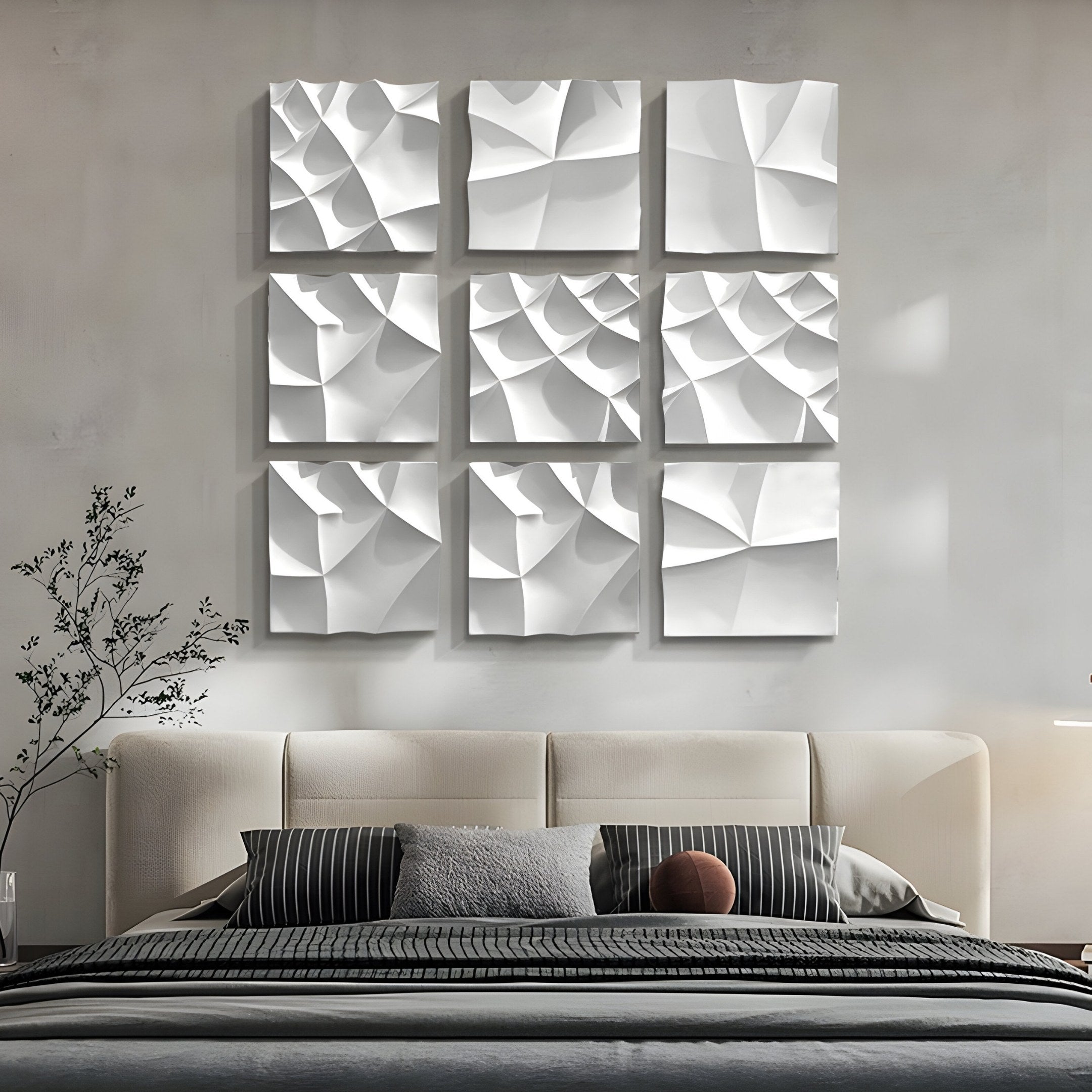 A modern bedroom showcases a beige upholstered bed with striped pillows and a cushion. Above the bed, Giant Sculptures Tessara I White 3D Wood Relief Wall Art forms a 3x3 grid of abstract patterns. Minimalist decor is enhanced by a slender plant on the left.