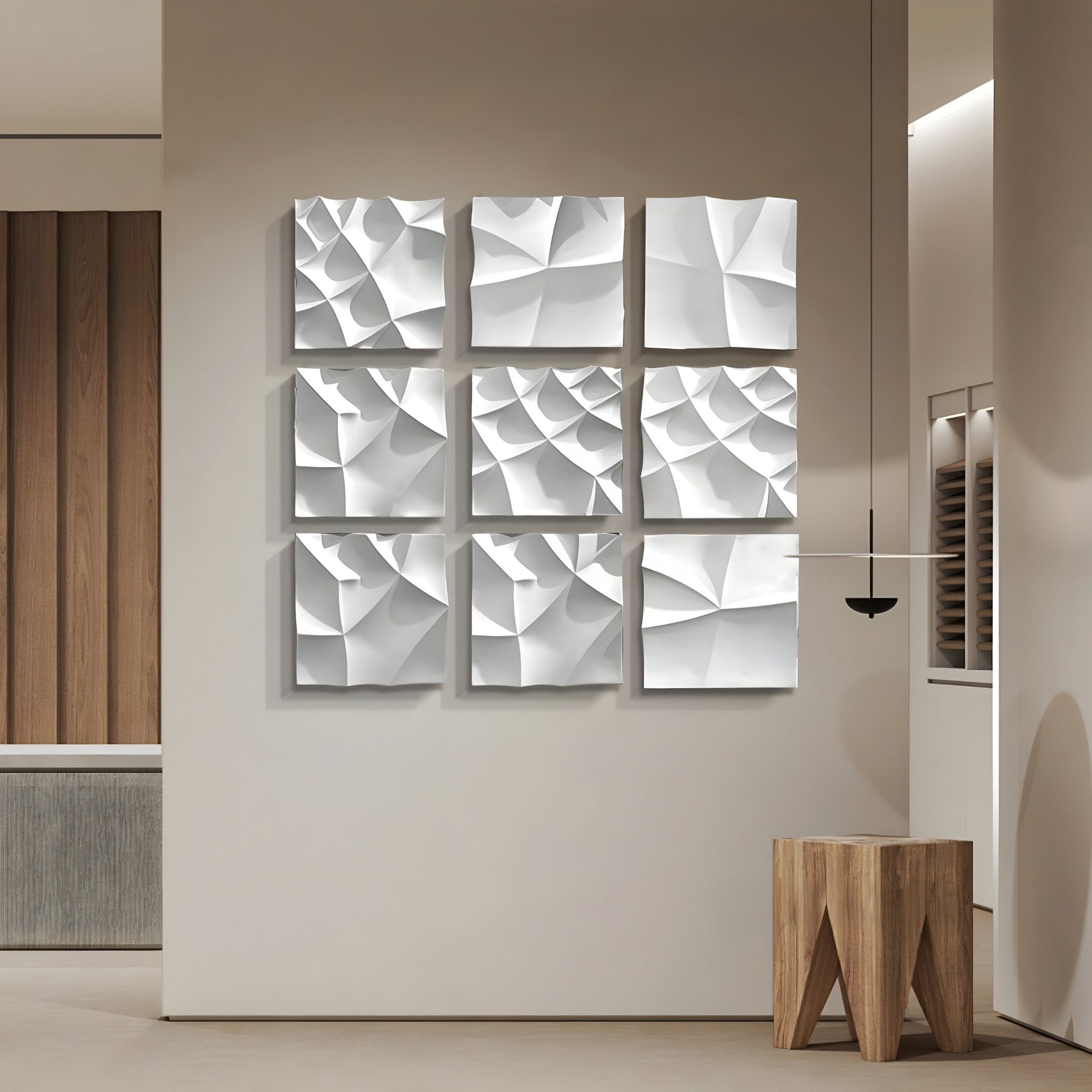 A minimalist room features the Tessara 9-Panel Set White 3D Wood Relief Wall Art by Giant Sculptures, forming an abstract geometric grid. A wooden stool and hanging light enhance the neutral walls and floor.