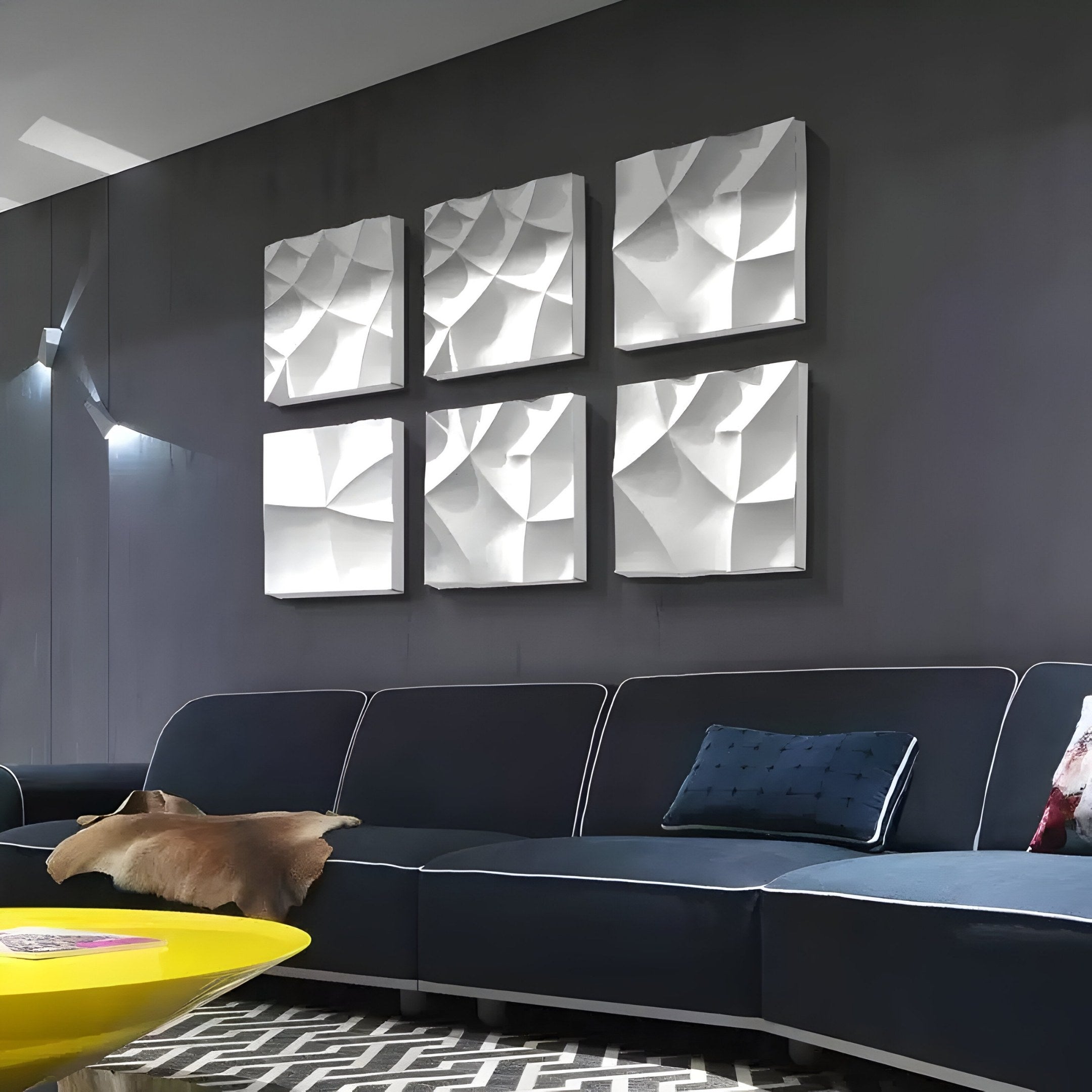 Modern living room with dark gray walls showcasing six Giant Sculptures Tessara 6-Panel White 3D Wood Relief Wall Art. A dark sectional sofa with a blue cushion and beige throw blanket faces a yellow coffee table on a geometric-patterned rug, enhancing the monochrome décor.