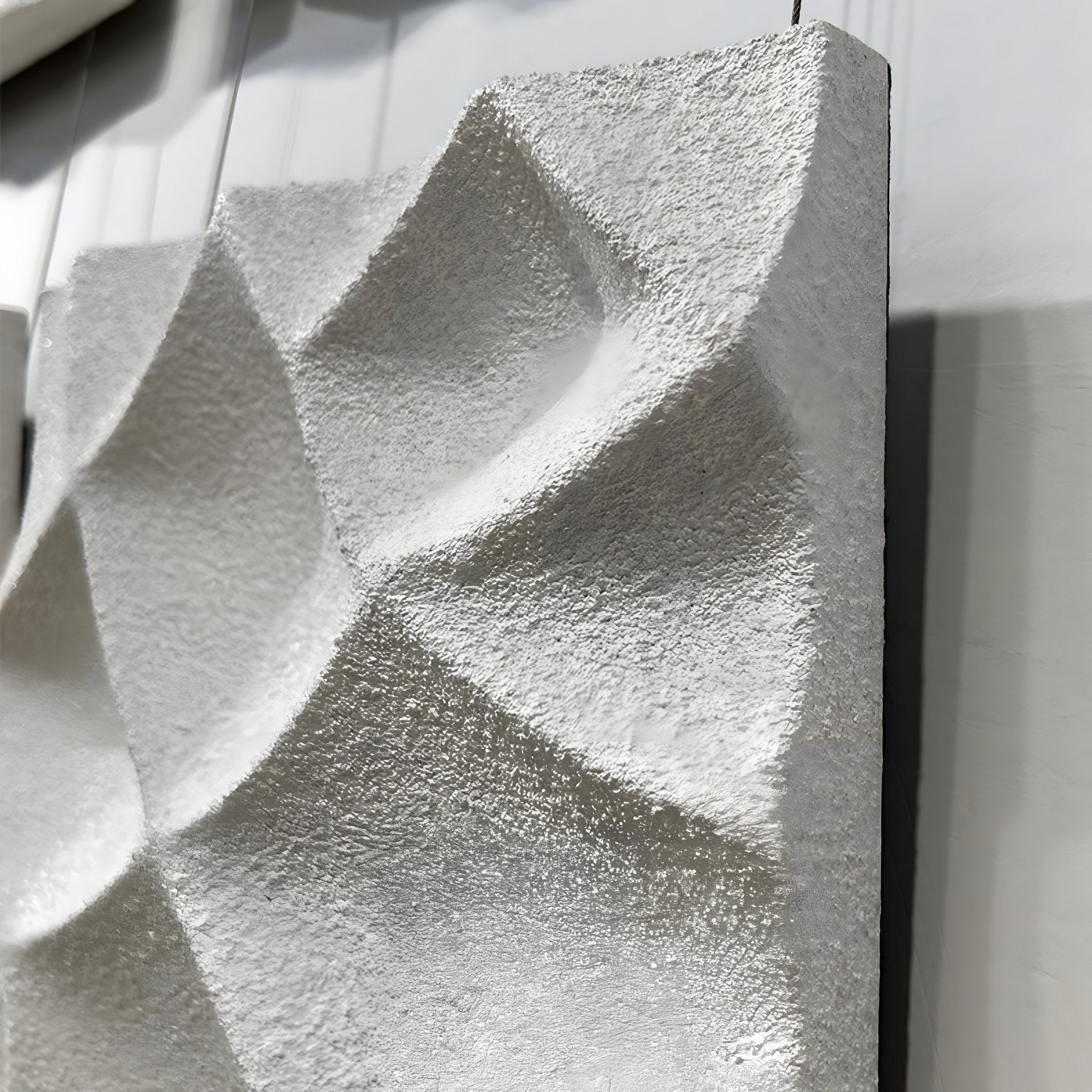 A close-up of the Tessara II White 3D Wood Relief Wall Art by Giant Sculptures reveals raised, angular shapes on a textured panel. Its rough, white surface is beautifully highlighted by lighting that accentuates shadows and geometric design.