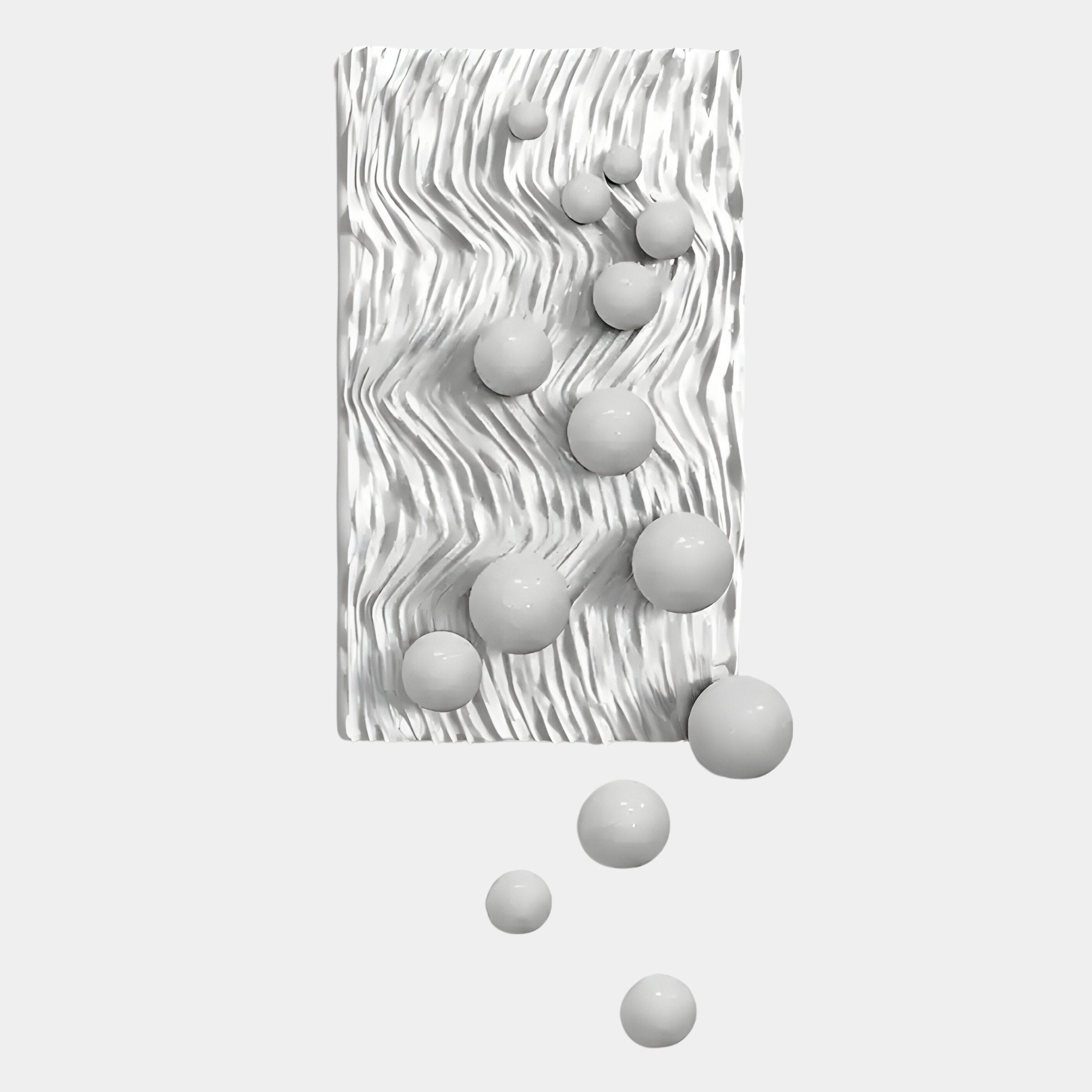 The Fluxion White 3D Wood Relief Wall Art With Metal Ball by Giant Sculptures showcases a rectangular white textured surface with glossy metal spheres in varying sizes set atop and below, some appearing to roll off onto the background.
