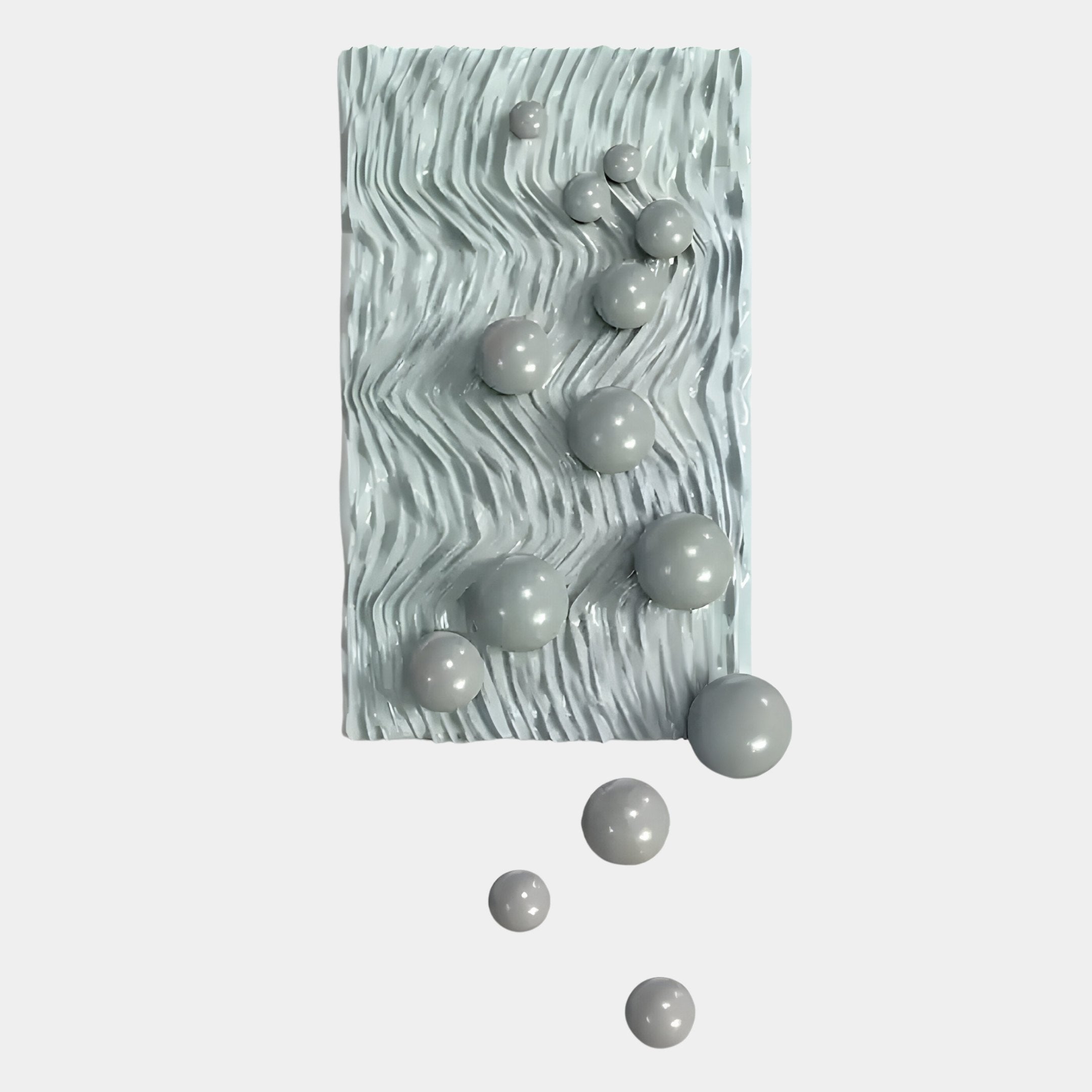 The Fluxion Muted Grey 3D Wood Relief Wall Art With Metal Ball by Giant Sculptures features a rectangular white textured panel with wavy grooves and glossy, muted grey metal-like spheres clustered near the center and lower edge.