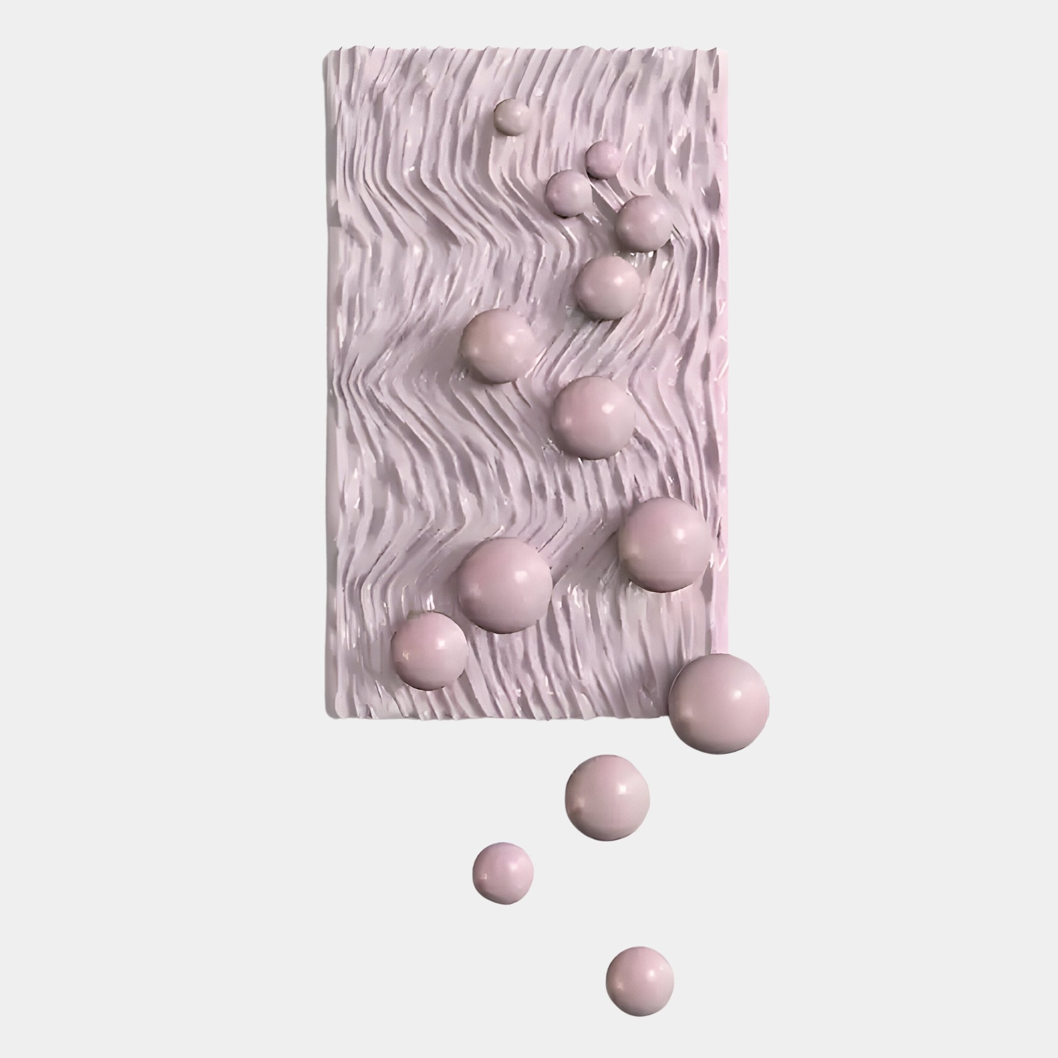 The Fluxion Soft Pink 3D Wood Relief Wall Art by Giant Sculptures features a rectangular, textured panel with wavy lines and glossy pastel pink metal balls in varying sizes—some extending past the edge onto a white background.