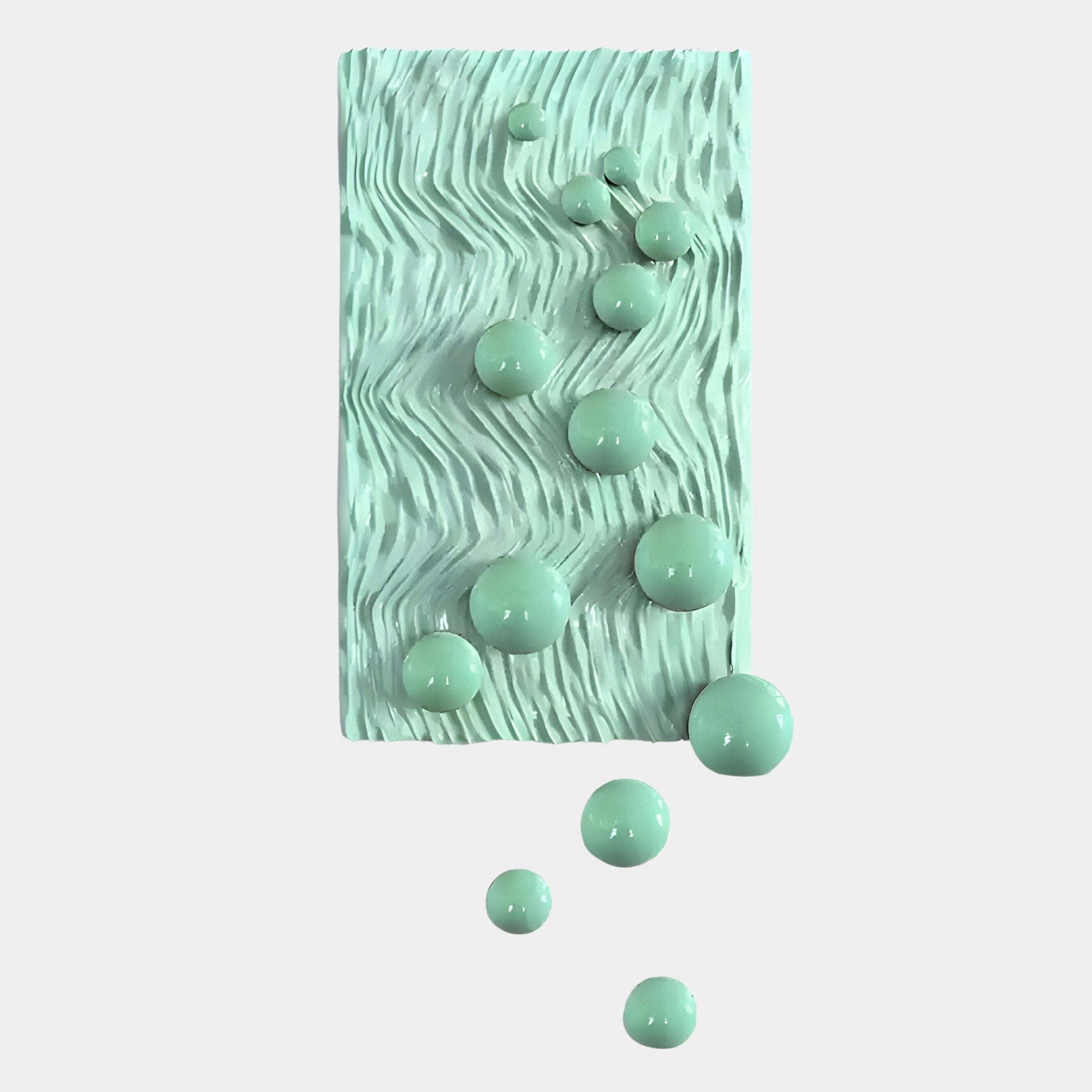 The Fluxion Mint Green 3D Wood Relief Wall Art With Metal Ball by Giant Sculptures features a mint-green panel with wavy grooves and glossy, rounded metal spheres of varying sizes cascading across a plain white background.