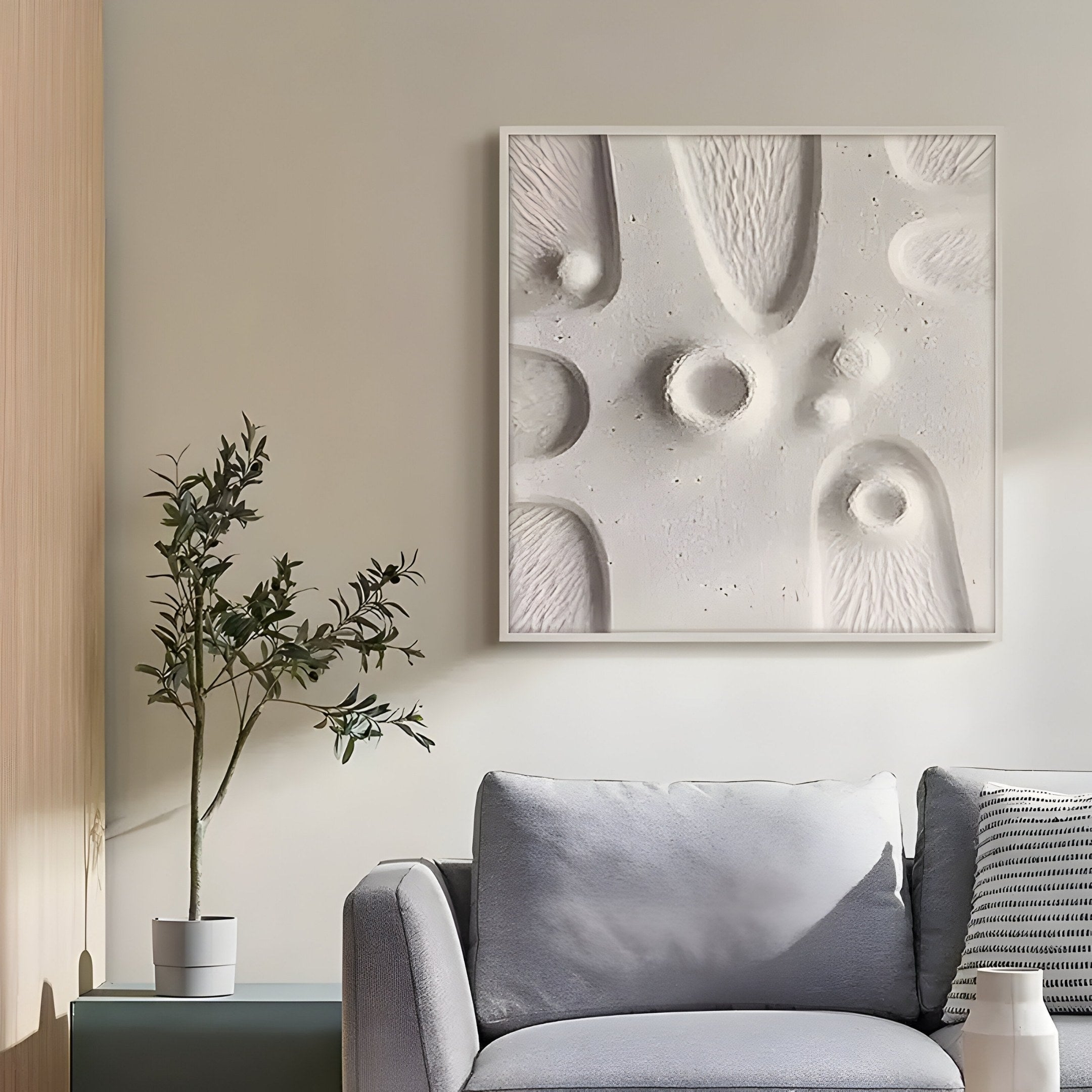 A minimalist living room features a light grey couch with cushions, a potted plant on a small table, and Giant Sculptures Terravura Square Soft White II 3D Wood Relief Wall Art above the couch, displaying abstract shapes. Natural light enhances the minimalist décor.