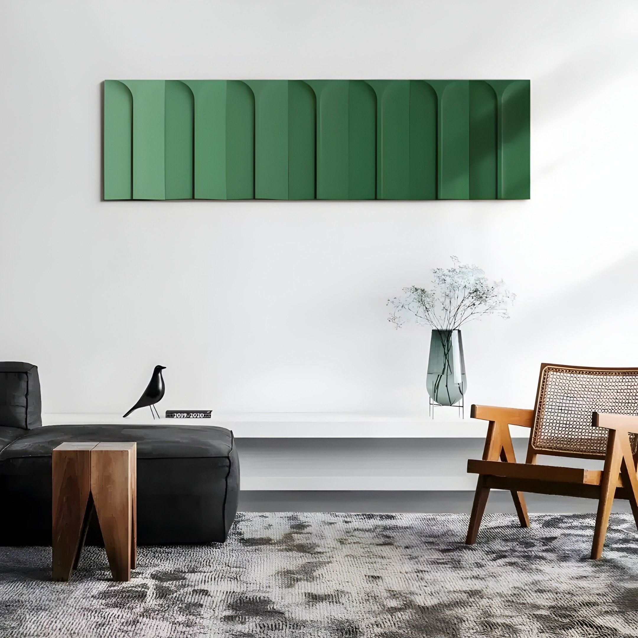 A modern living room with minimalist decor features Giant Sculptures Vireus Green Single Panel 3D Wood Relief Wall Art on a white wall. A black sofa and wooden chair complement the space, while a bird sculpture sits on a low white table with a glass vase of white flowers accentuating the design.