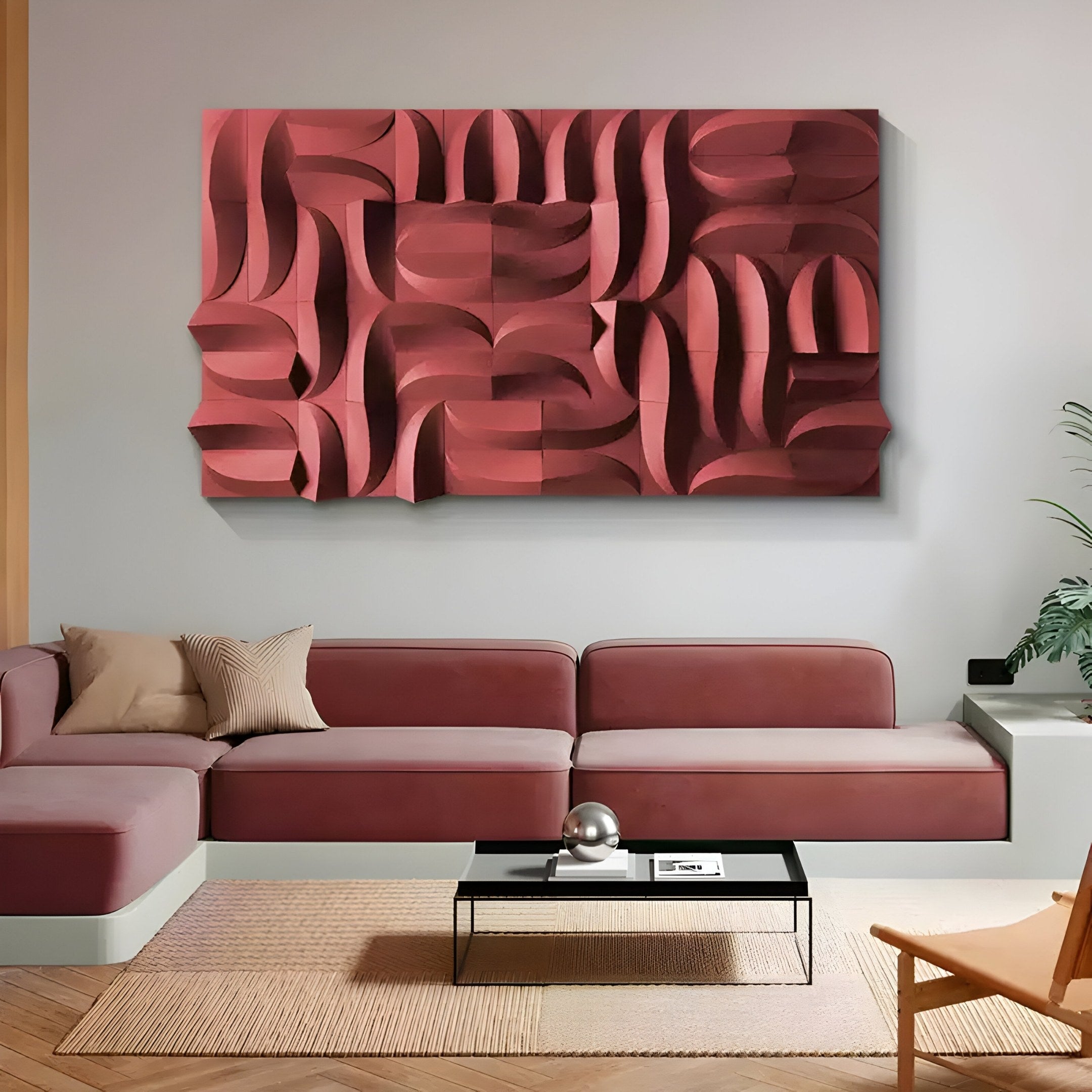 A modern living room features a pink sectional sofa, a black coffee table with a silver ornament, and the Ombra Burgundy Hand-Painted Sandstone 3D Wood Relief Wall Art by Giant Sculptures. A woven rug covers the floor, and a small plant in the corner adds life to the space.