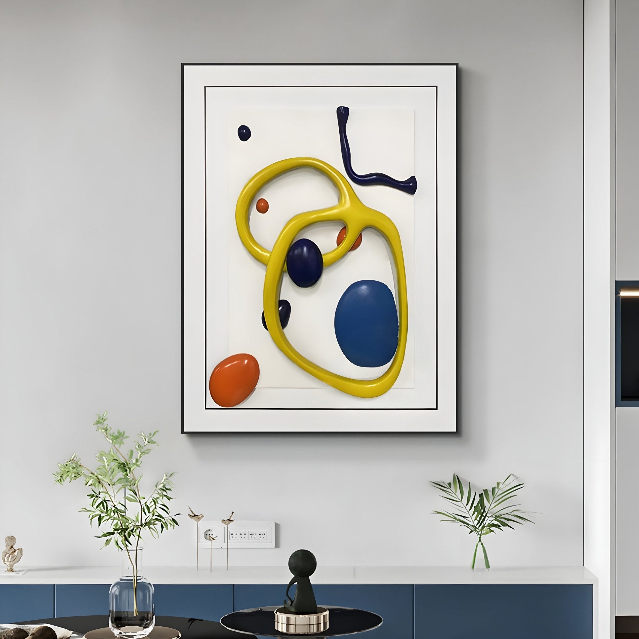 The Vitrus Yellow & Blue Abstract Wood Embossed 3D Wall Art by Giant Sculptures adorns a light gray wall, showcasing bold yellow, blue, and orange shapes. Below, a blue cabinet displays small plants and decor. The artworks 3D effect adds depth and vibrancy to the room.