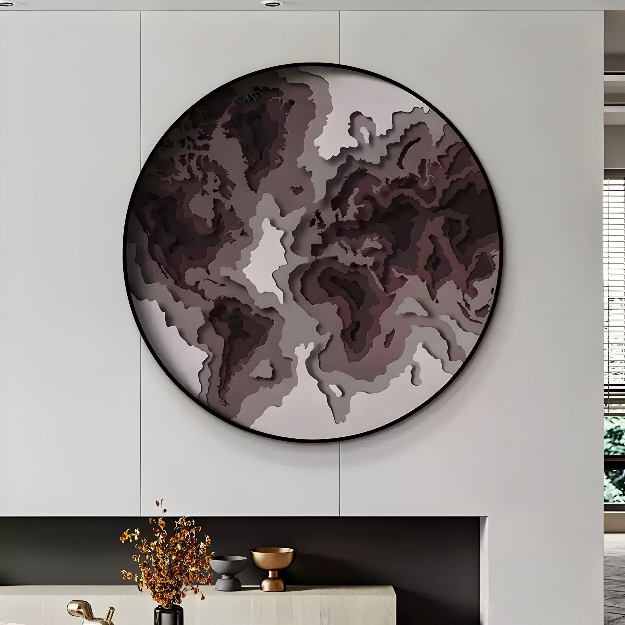 The Terranova Mocha Brown Round Wood Carving 3D Wall Art by Giant Sculptures hangs on a light-colored wall. Below, a shelf holds a small vase of dried orange flowers and two decorative bowls, with natural light filtering through a window on the right.