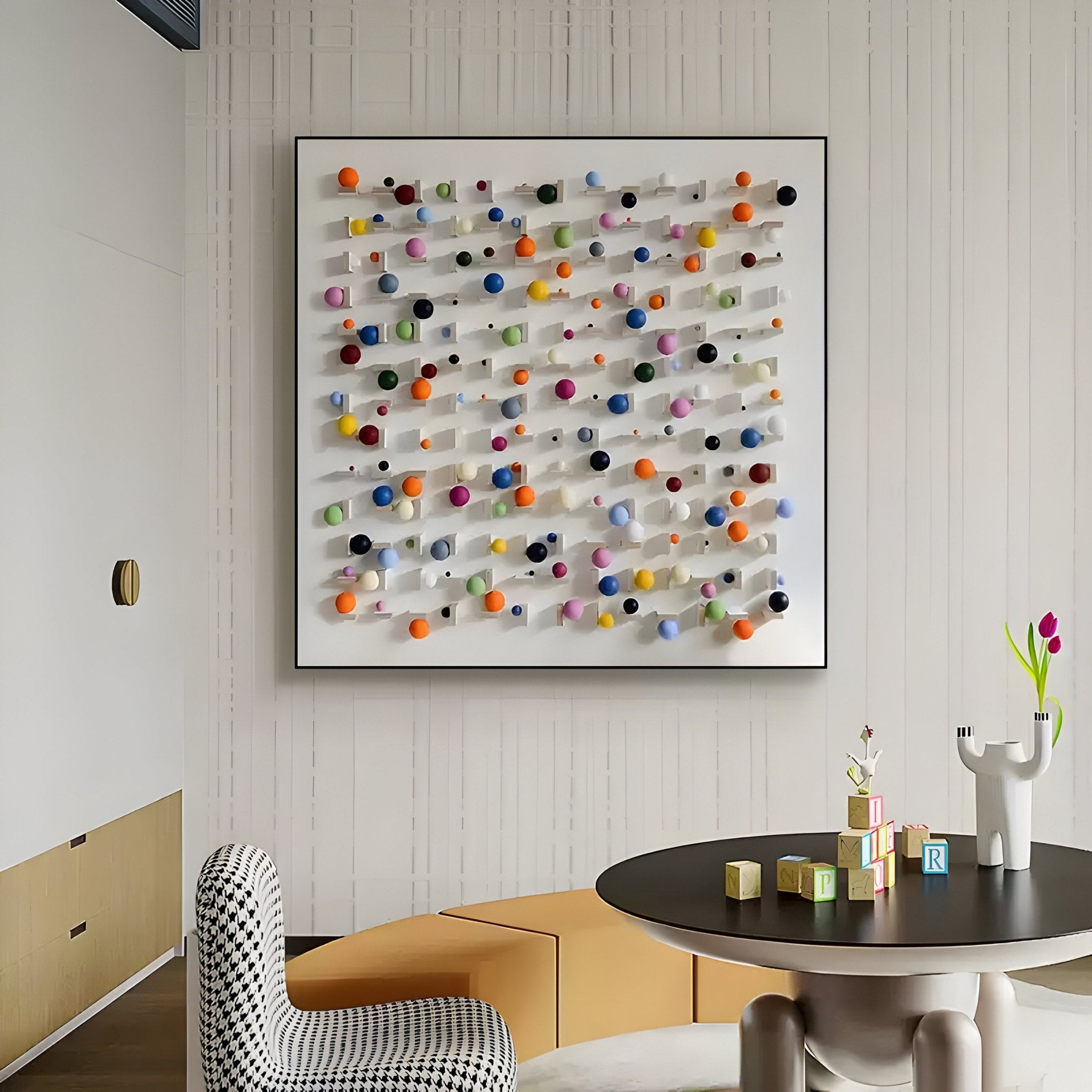 A modern room features Giant Sculptures Aeris Multi-Coloured Wooden Sphere 3D Wall Art in a grid pattern. A round table with childrens blocks and a playful vase of flowers stands in the foreground, alongside a checkered chair and rounded yellow seating completing the scene.